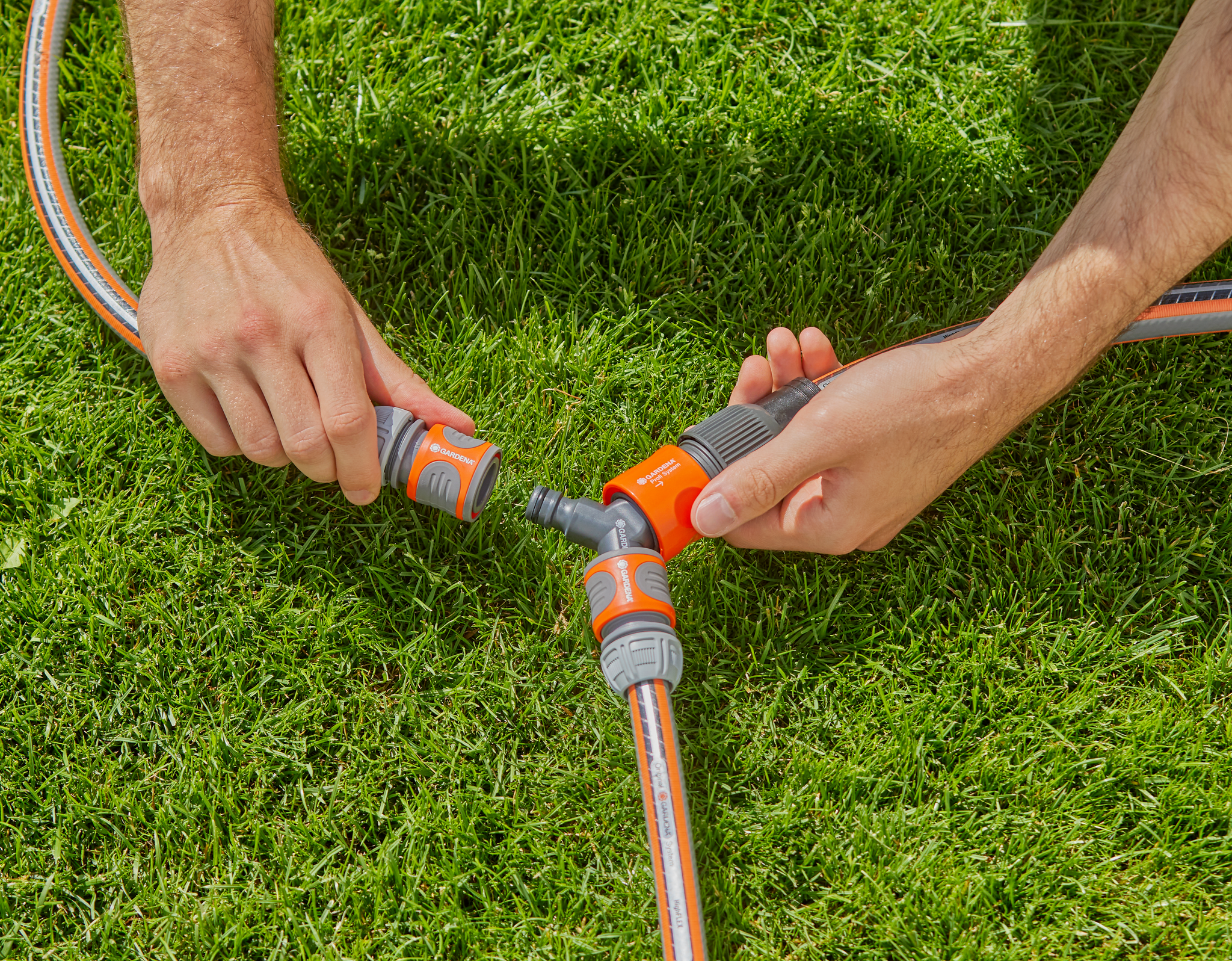 Hands connecting Gardena hose fittings on a grassy lawn.