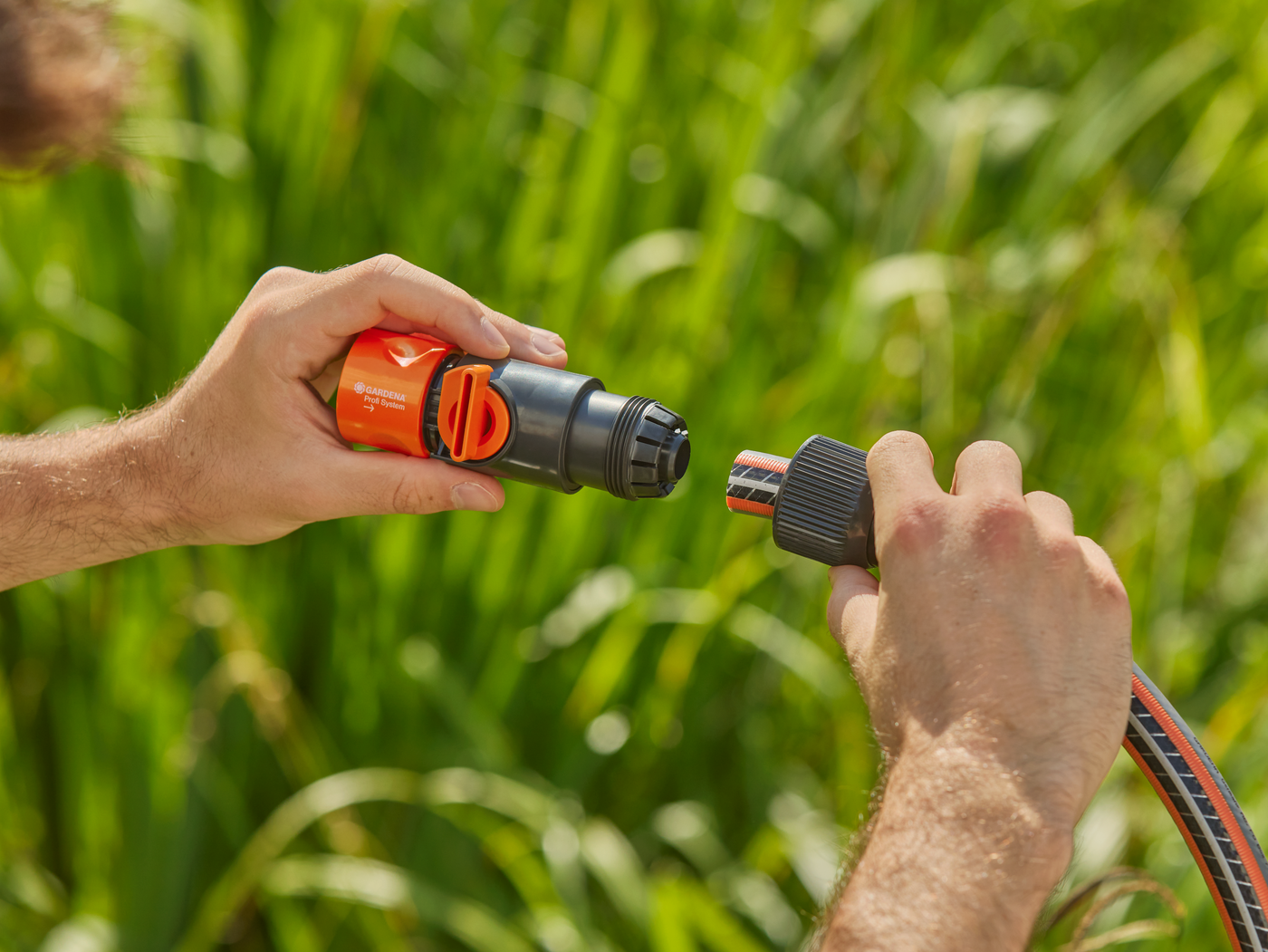 A person connecting a Gardena hose connector to a garden hose in a grassy area.