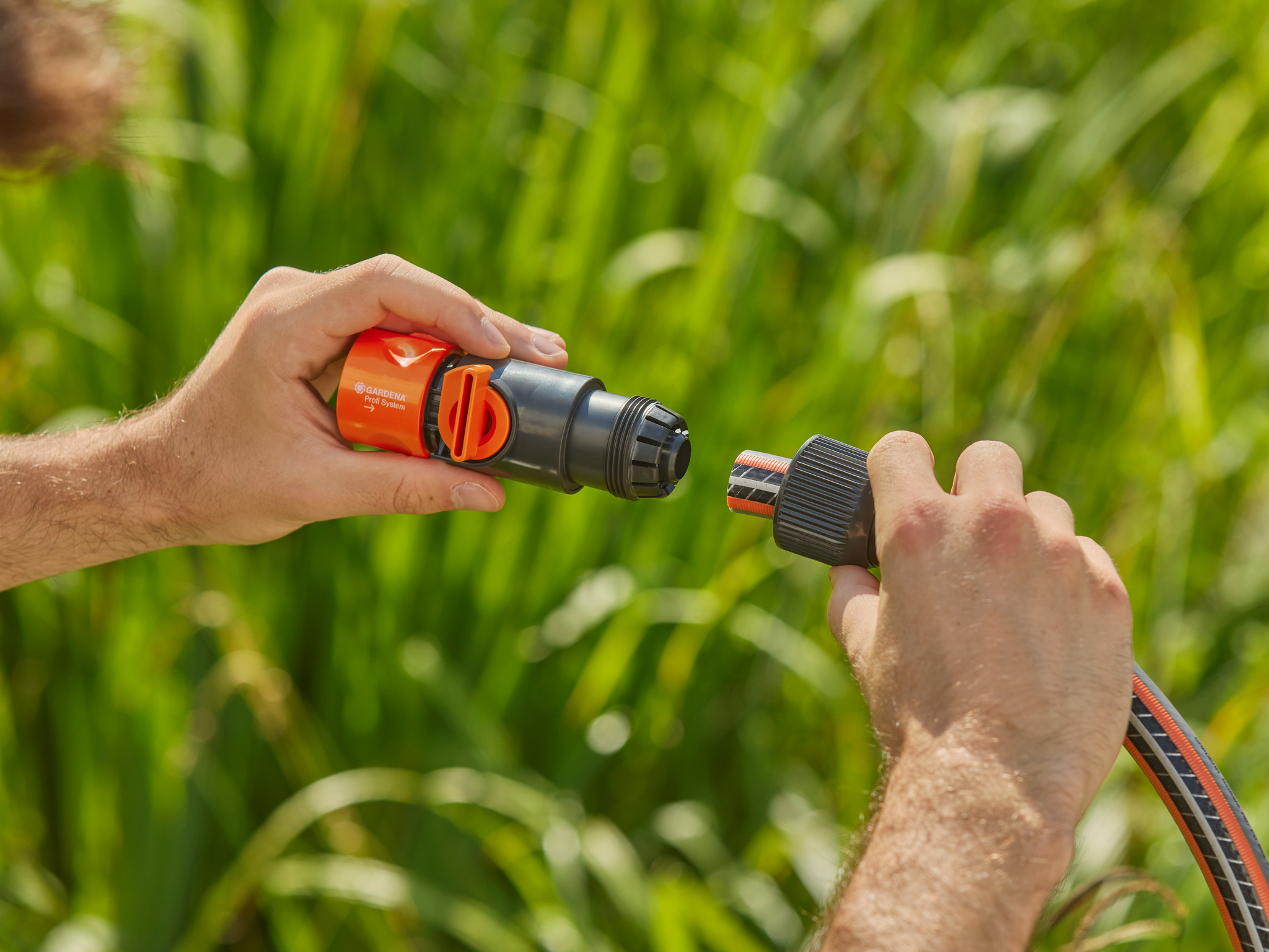 A person connecting a Gardena hose connector to a garden hose in a grassy area.