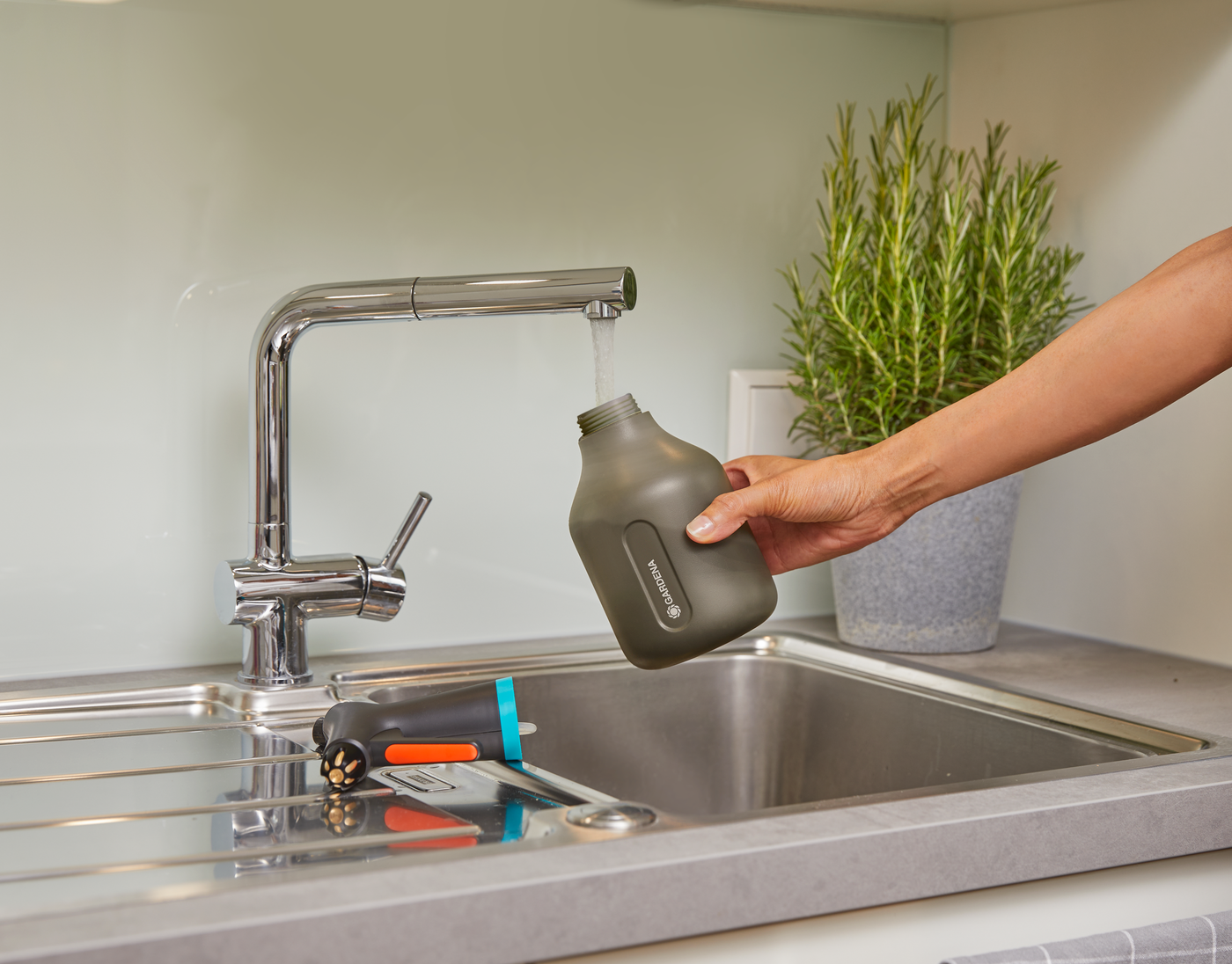 A person filling a Gardena water container at a kitchen sink.