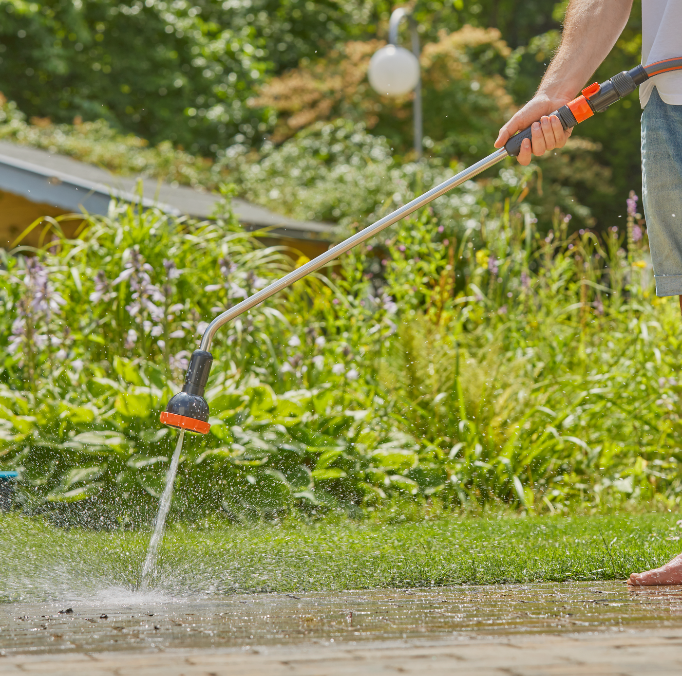 A person using a Gardena watering wand to water plants in a garden.
