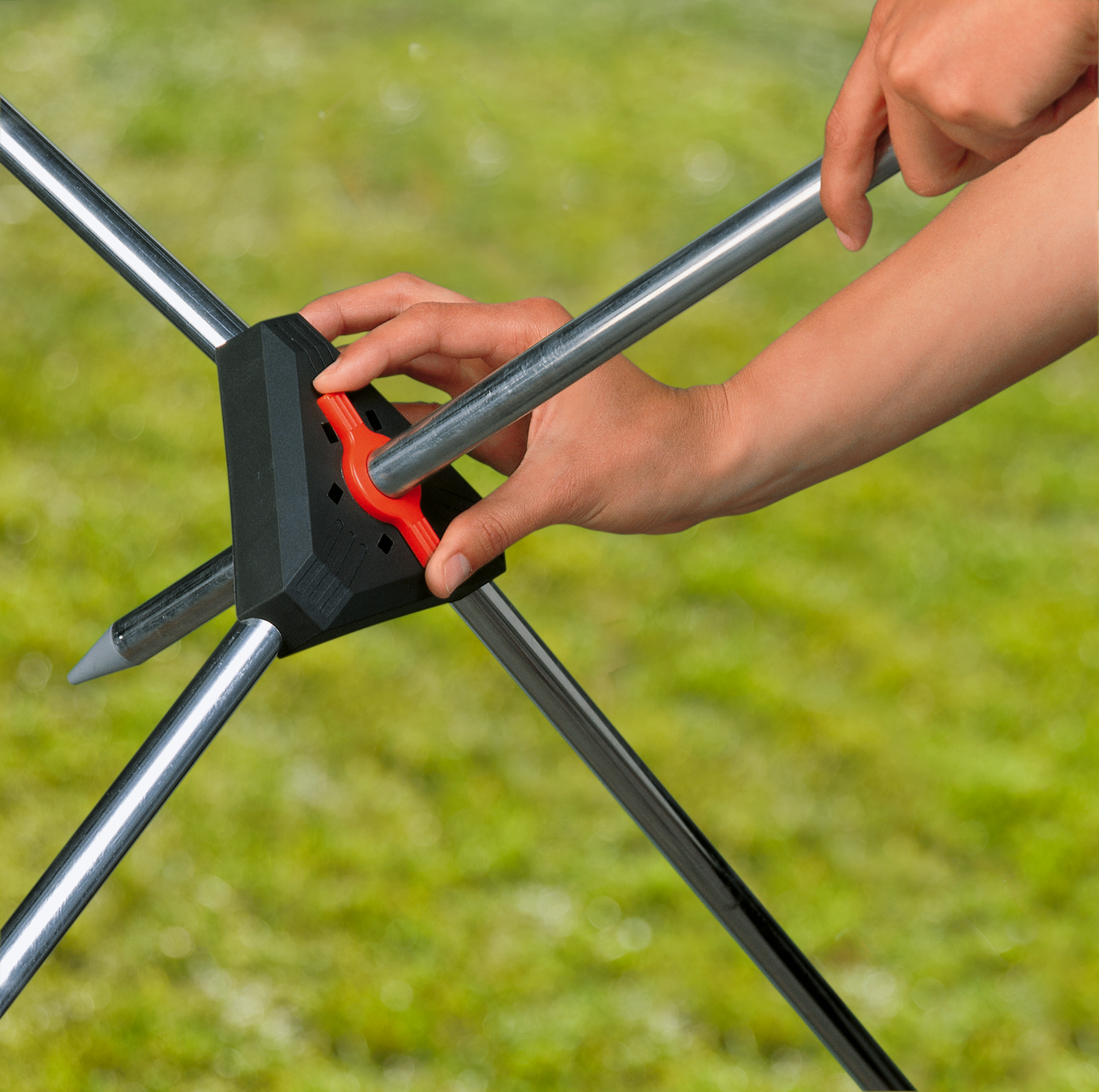 A person assembling a garden tool with metal rods and a central connector.