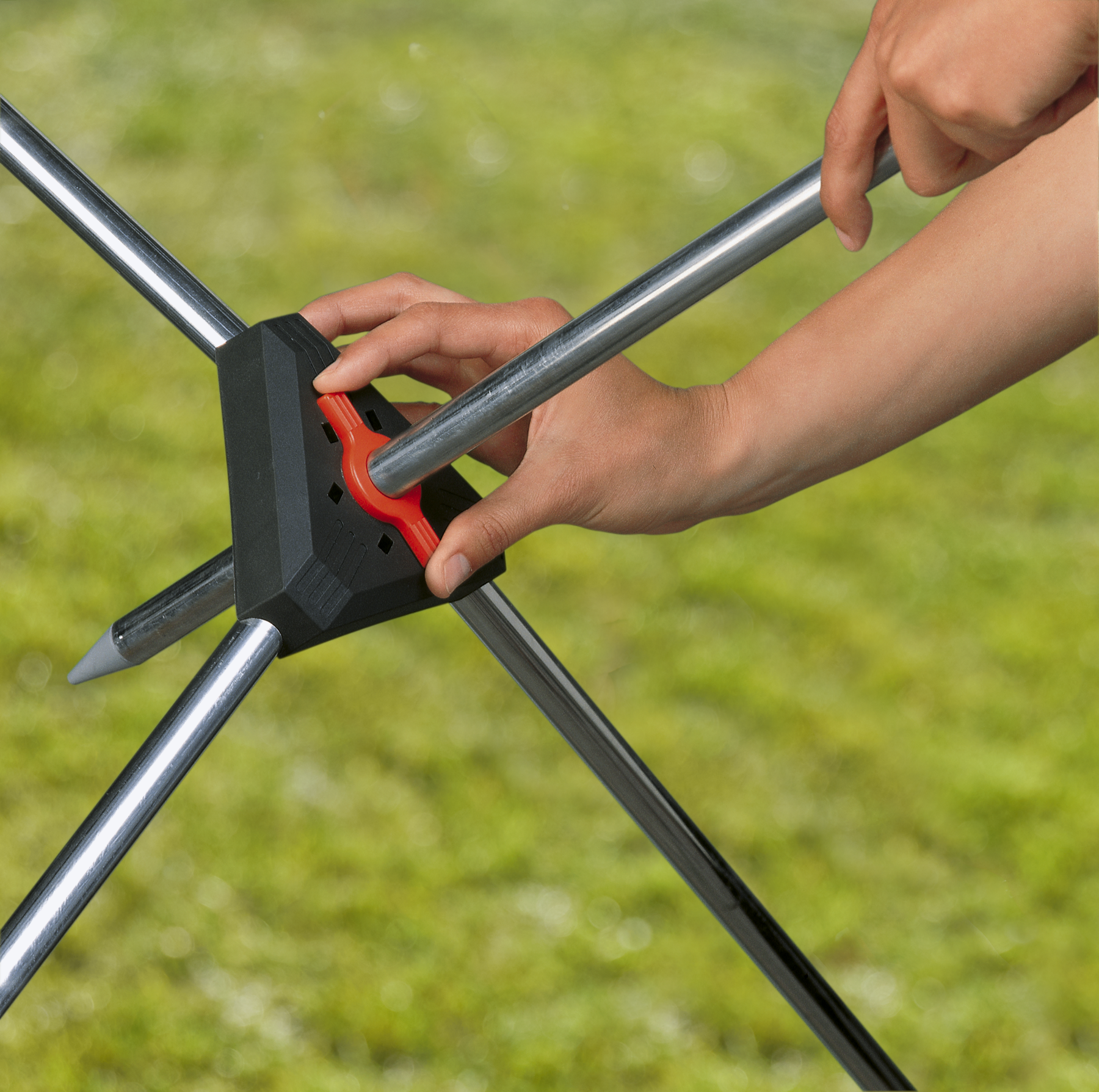 A person assembling a garden tool with metal rods and a central connector.