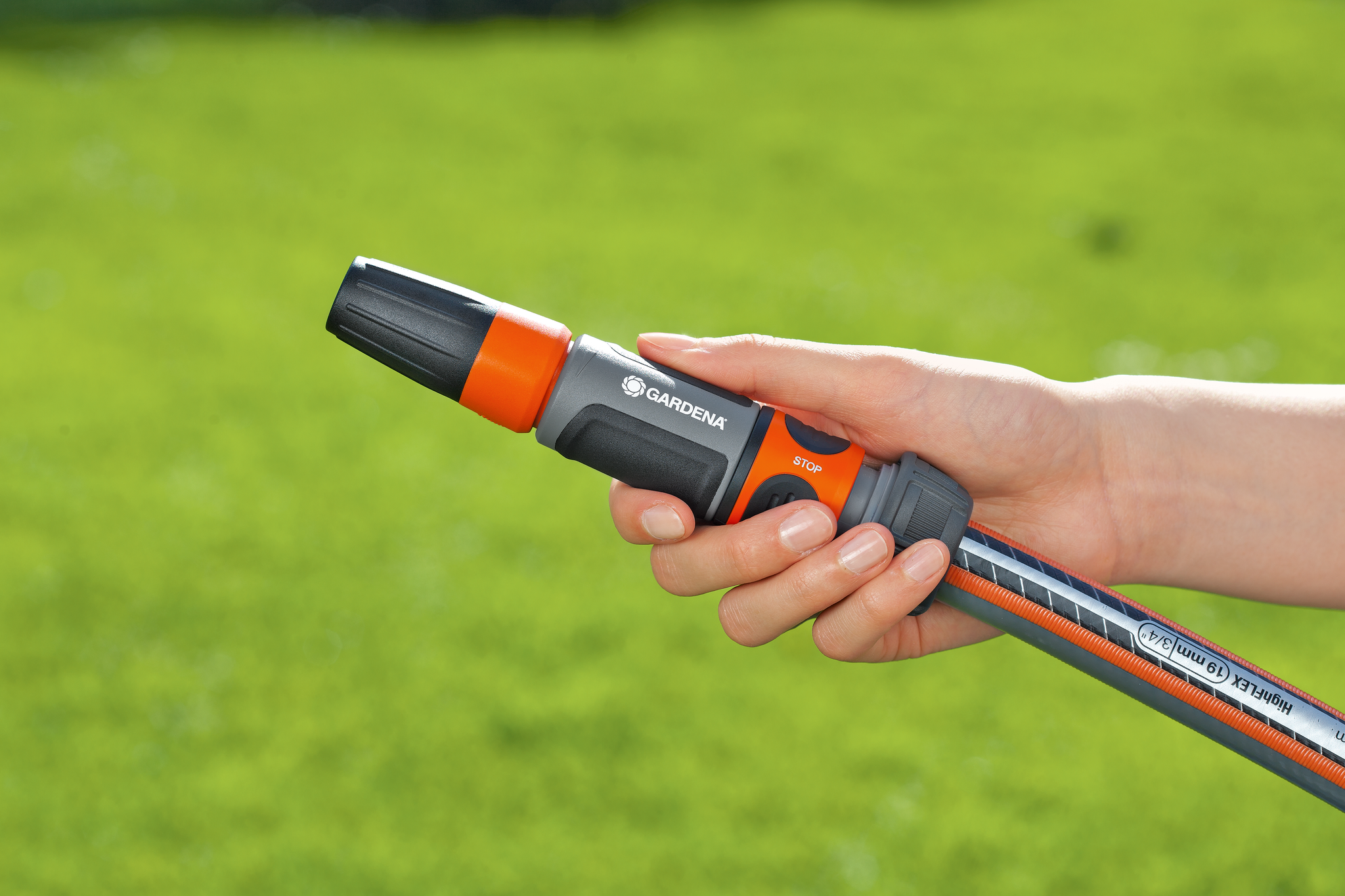 A hand holding a Gardena garden hose nozzle in a garden setting.