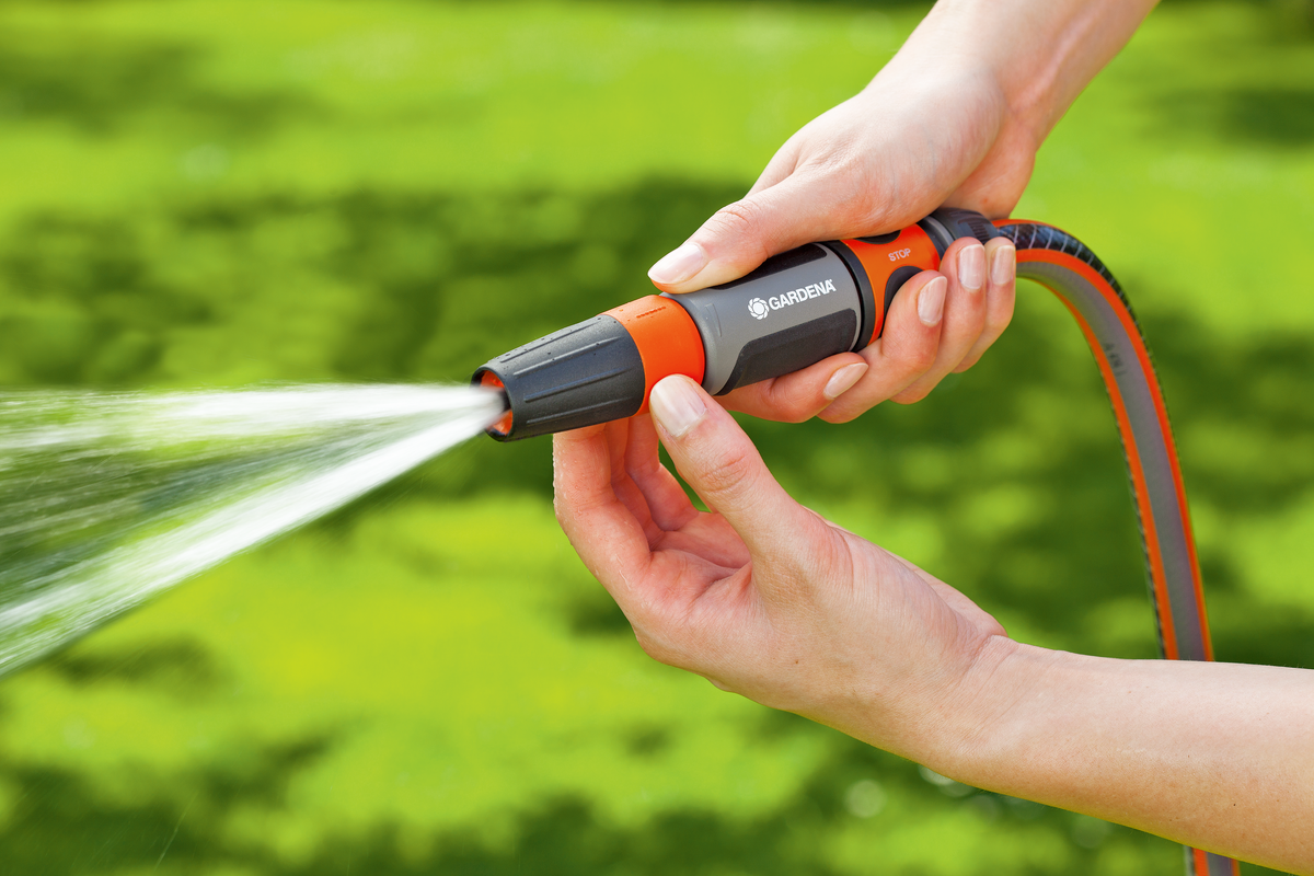 A person holding a Gardena garden hose nozzle, spraying water in a garden.