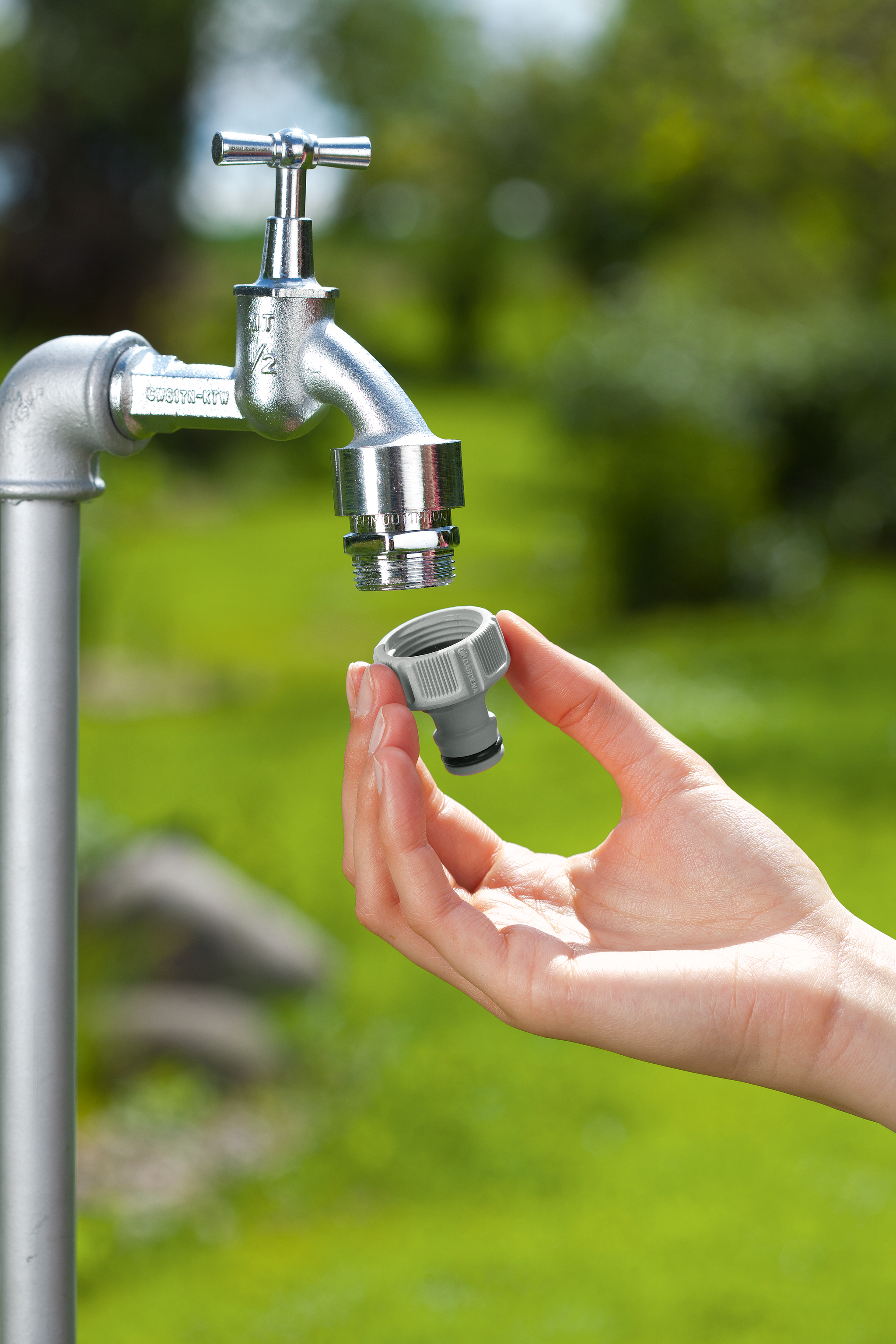 A person attaching a hose connector to an outdoor water tap in a garden.