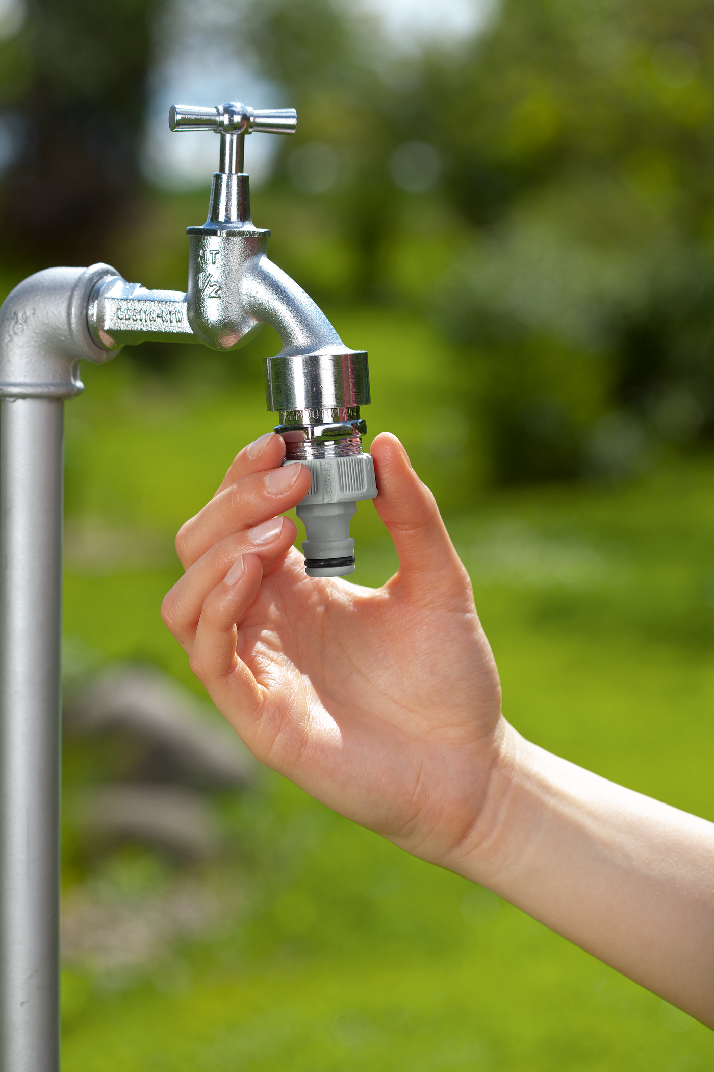 A hand attaching a Gardena hose connector to a garden tap outdoors.