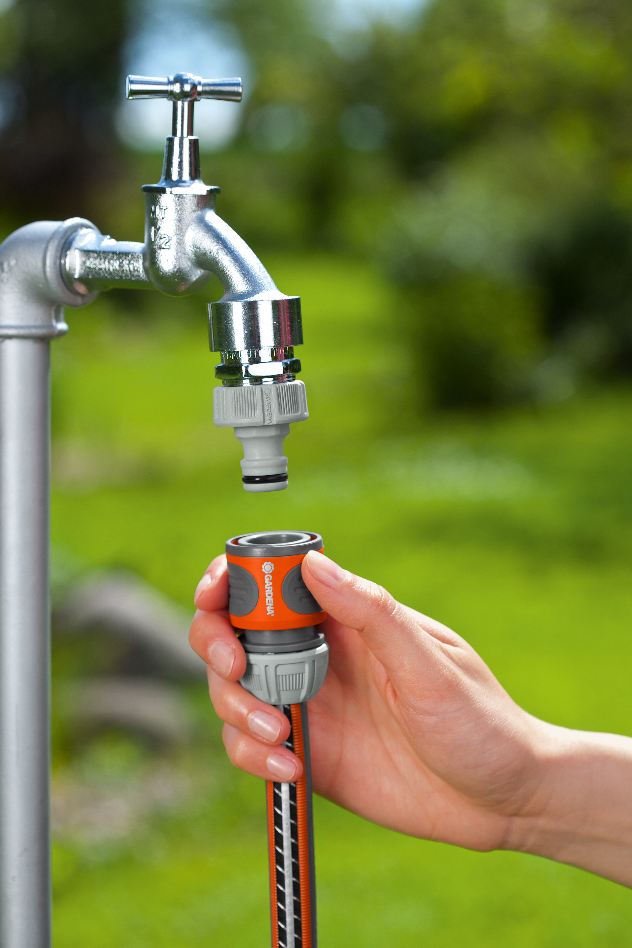 A person connecting a Gardena hose connector to a garden tap.