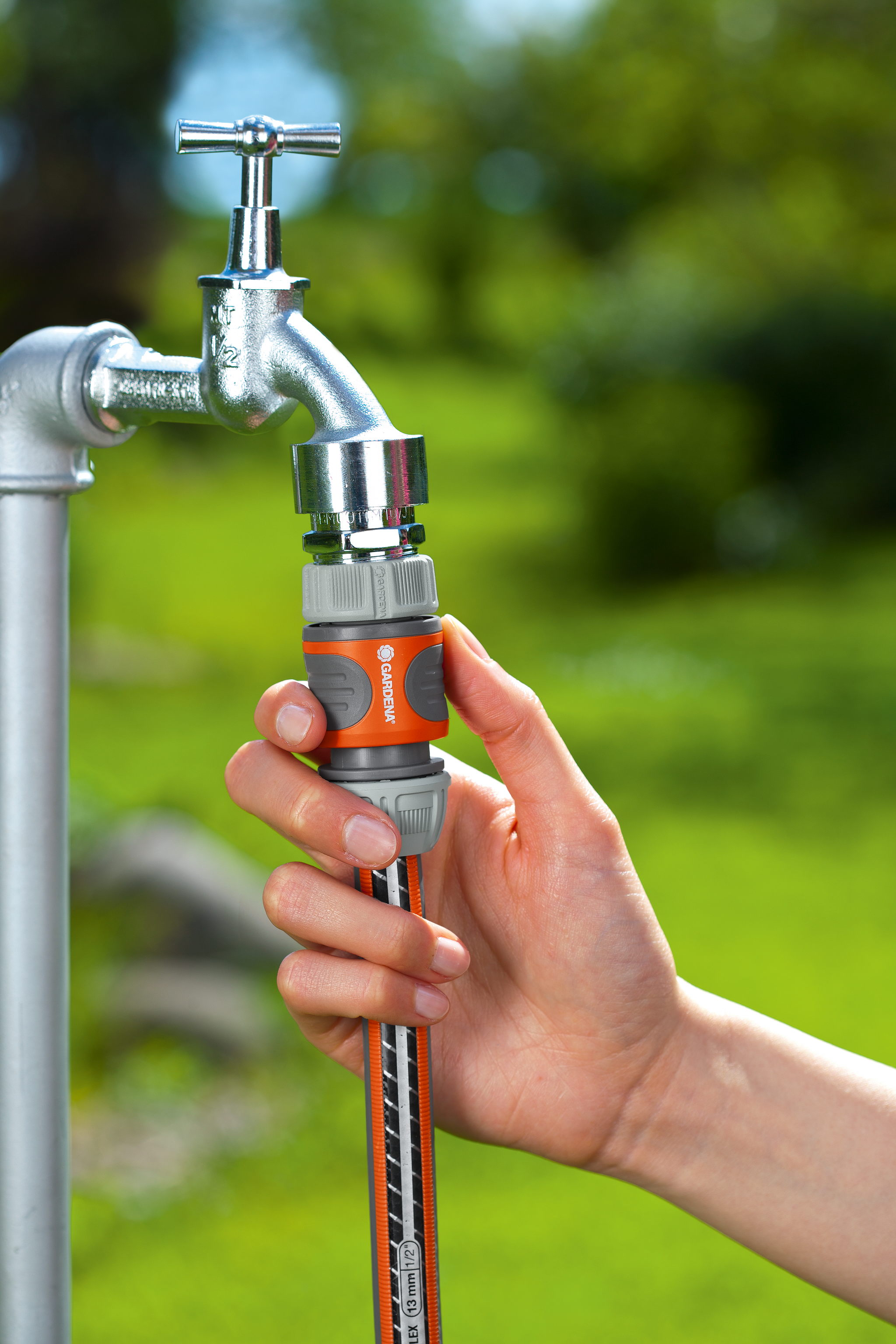 A person attaching a Gardena hose connector to an outdoor water tap.