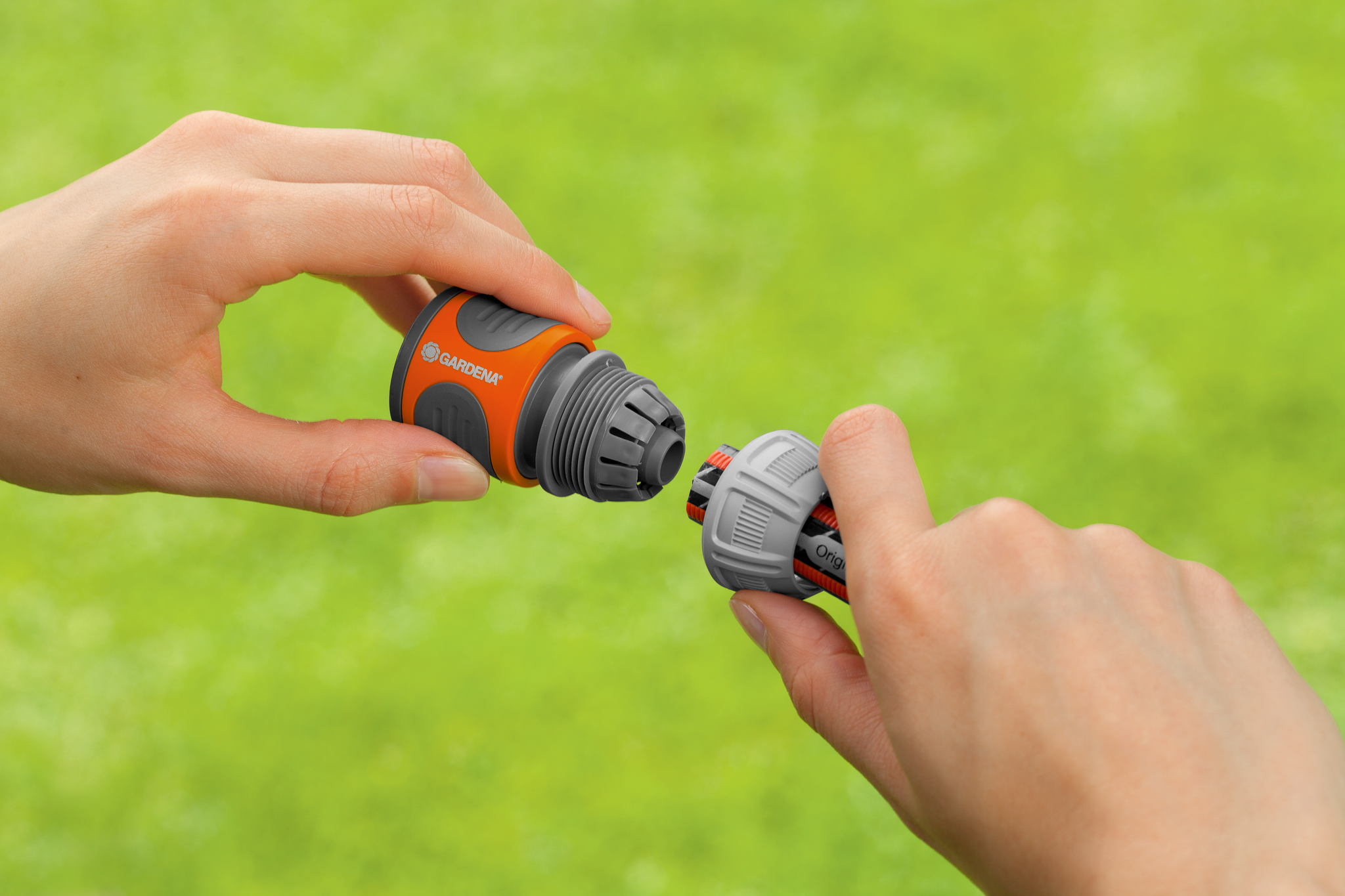 Two hands connecting Gardena hose accessories against a green background.