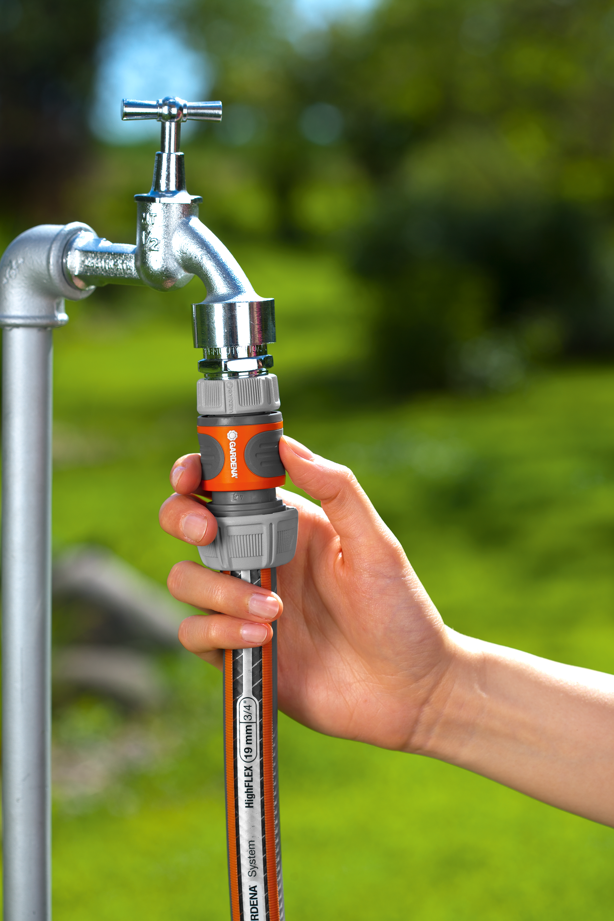 A hand attaching a Gardena hose connector to a garden tap.
