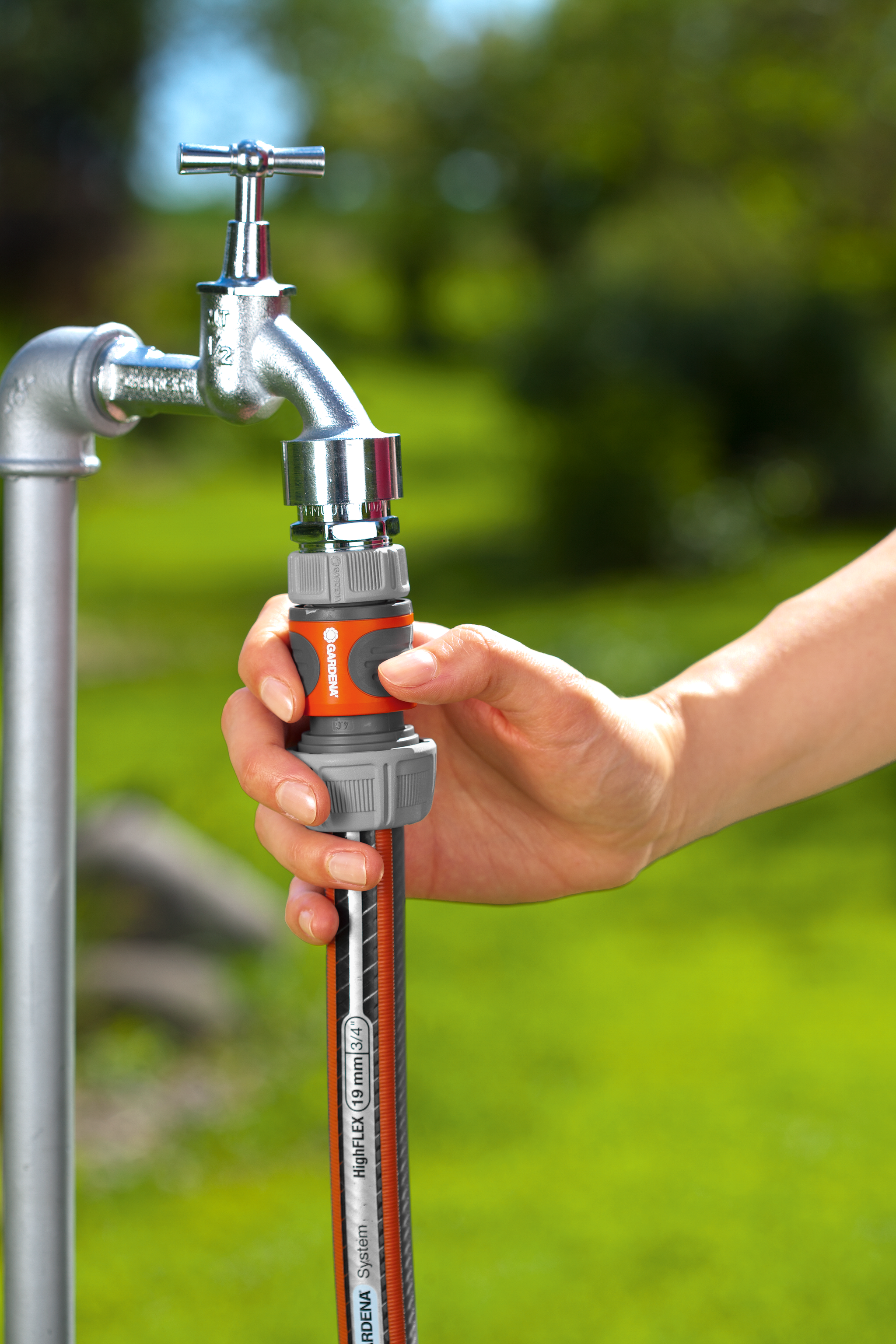 A person attaching a Gardena hose connector to an outdoor water tap.