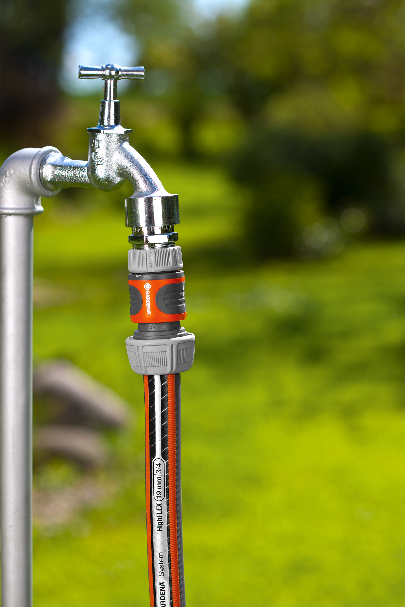 Gardena garden hose connected to an outdoor water tap in a garden setting.