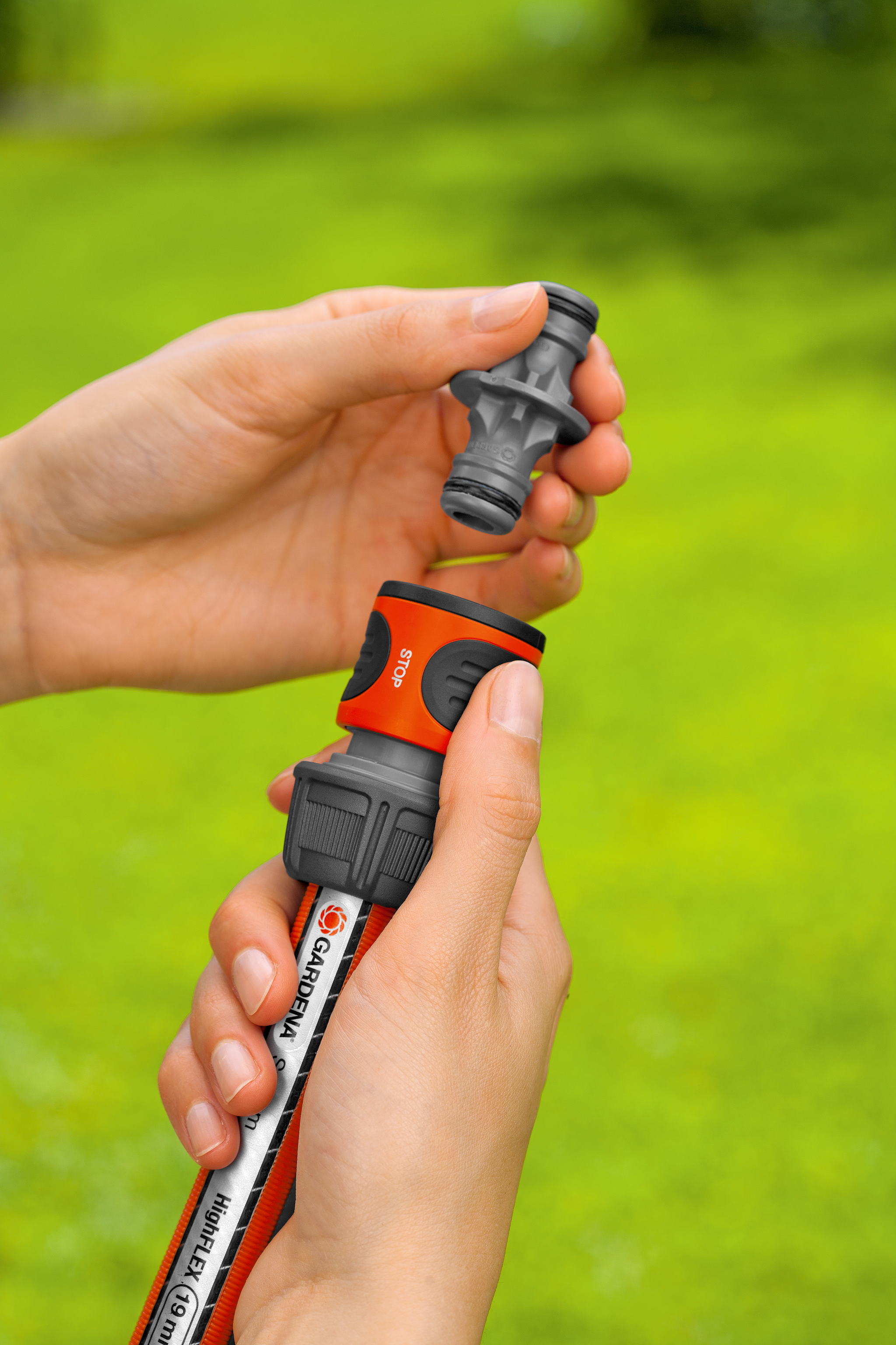 A person connecting a Gardena hose nozzle to a garden hose in a grassy area.
