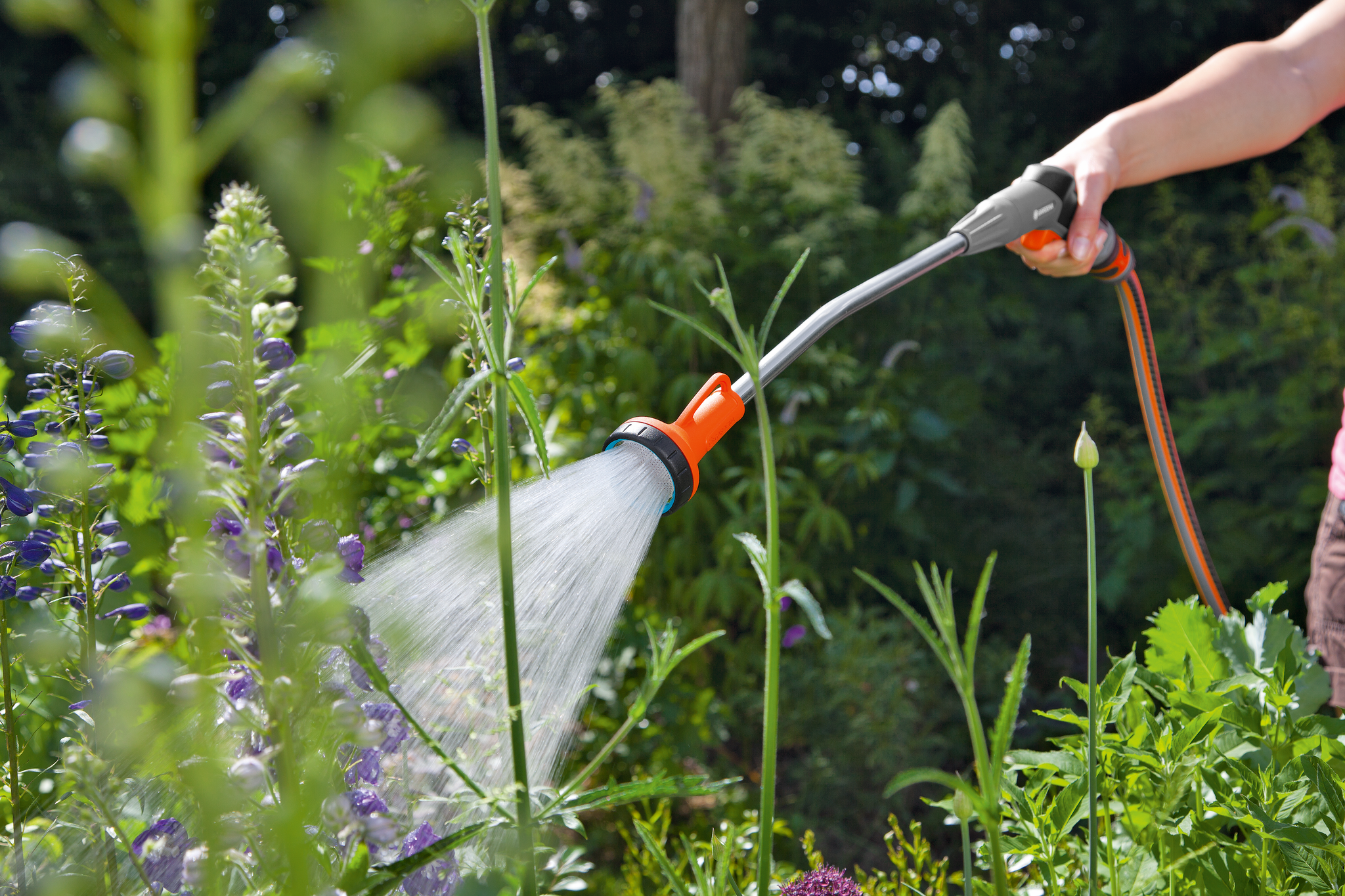 A person watering plants in a garden using a Gardena hose nozzle.