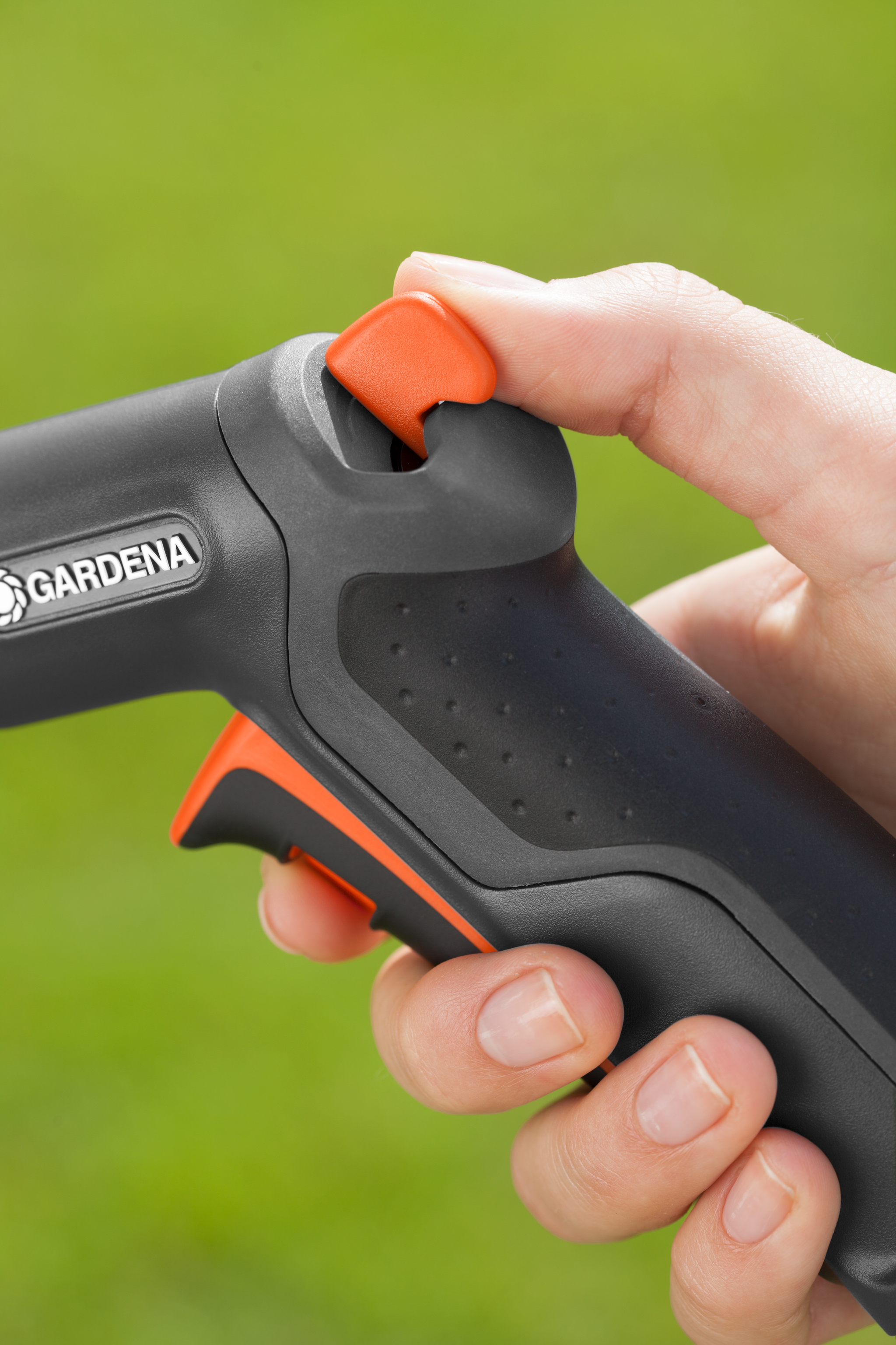 Close-up of a hand holding a Gardena garden tool handle with a thumb on the trigger.
