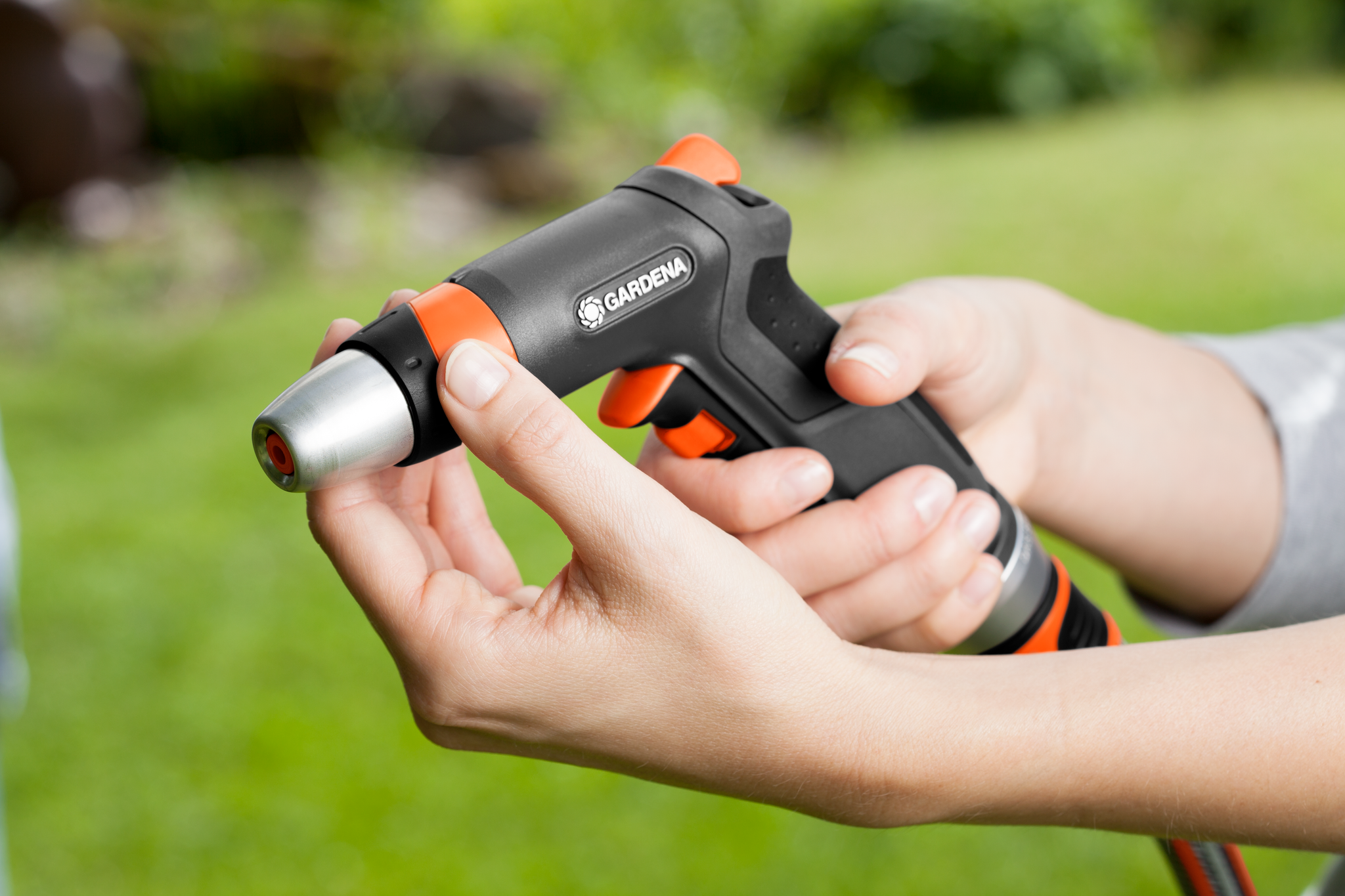 Close-up of hands adjusting a Gardena garden hose nozzle in a garden setting.