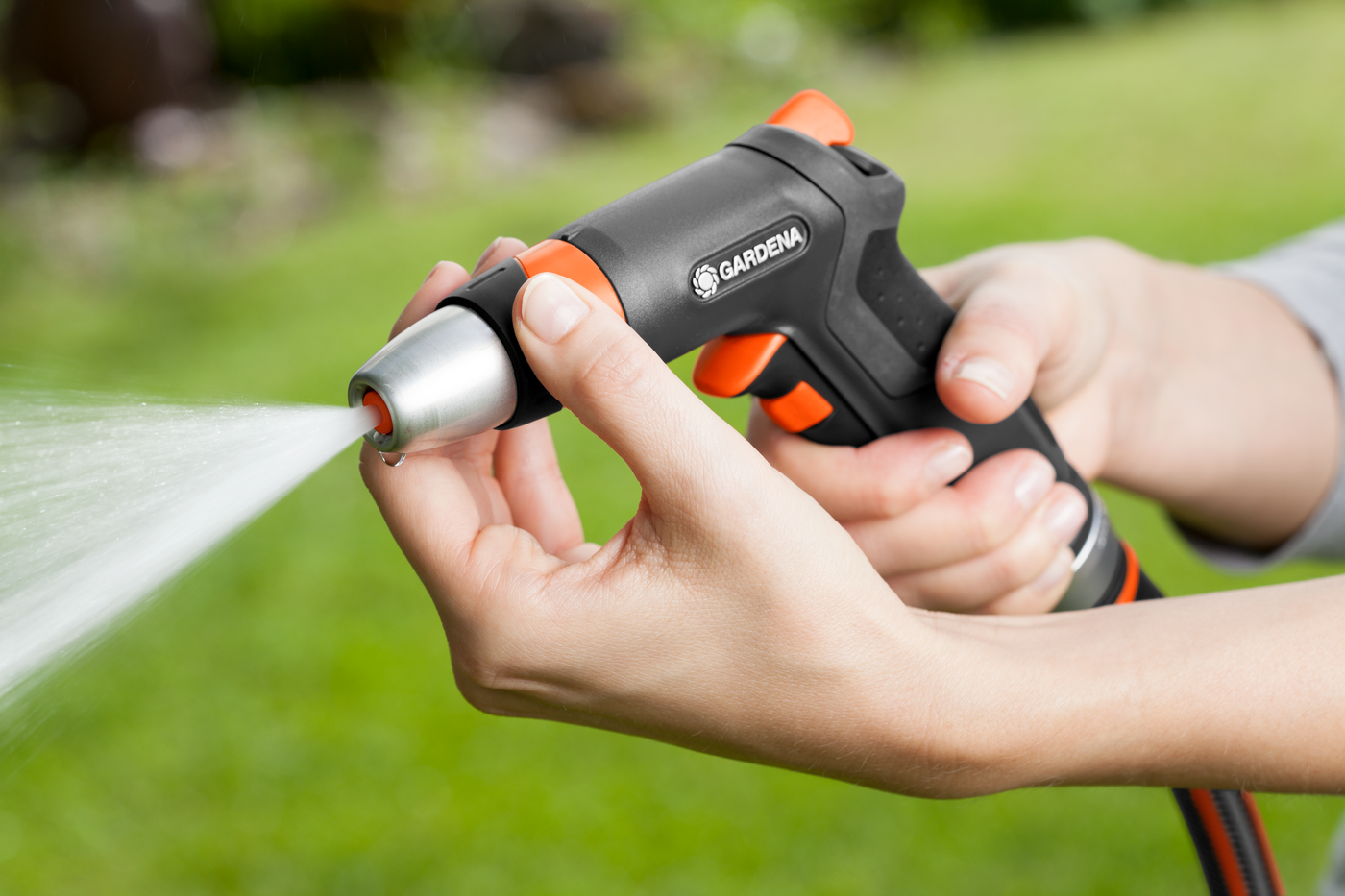 A person adjusting the nozzle of a Gardena garden hose sprayer, with water spraying out.