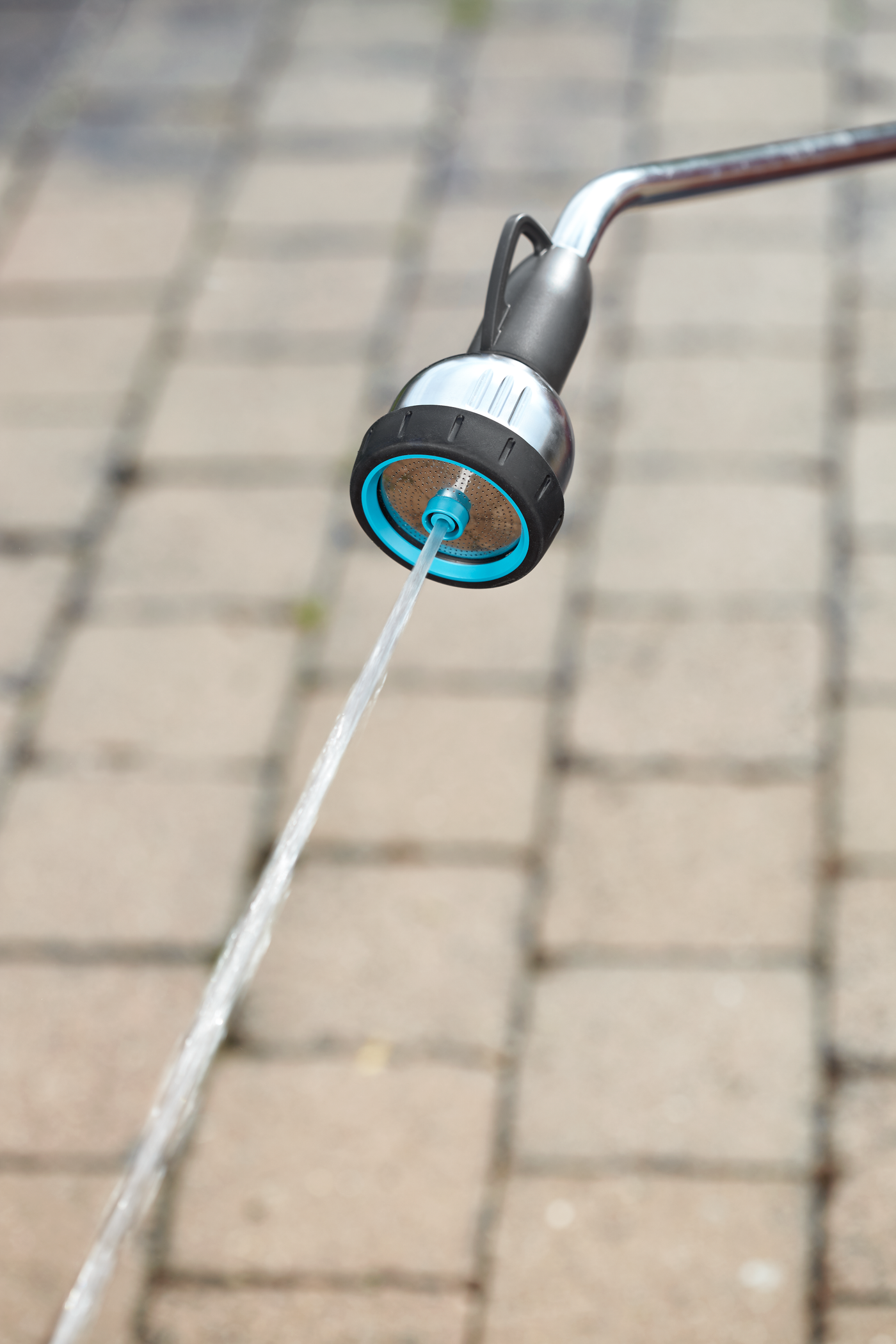 A close-up view of a garden hose nozzle spraying water onto a paved surface.