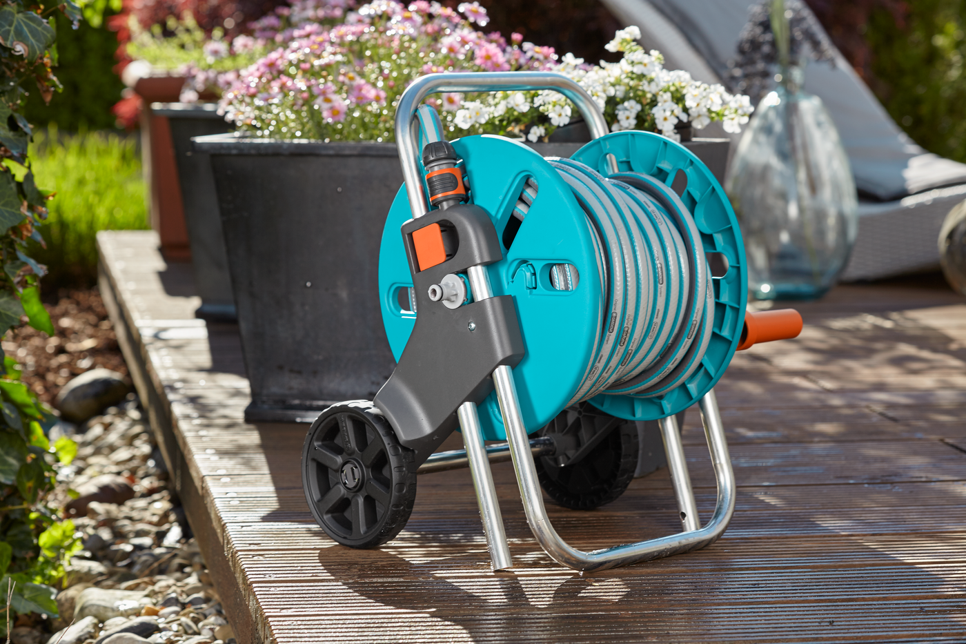 Gardena hose reel with a garden hose, placed on a wooden deck next to potted flowers.