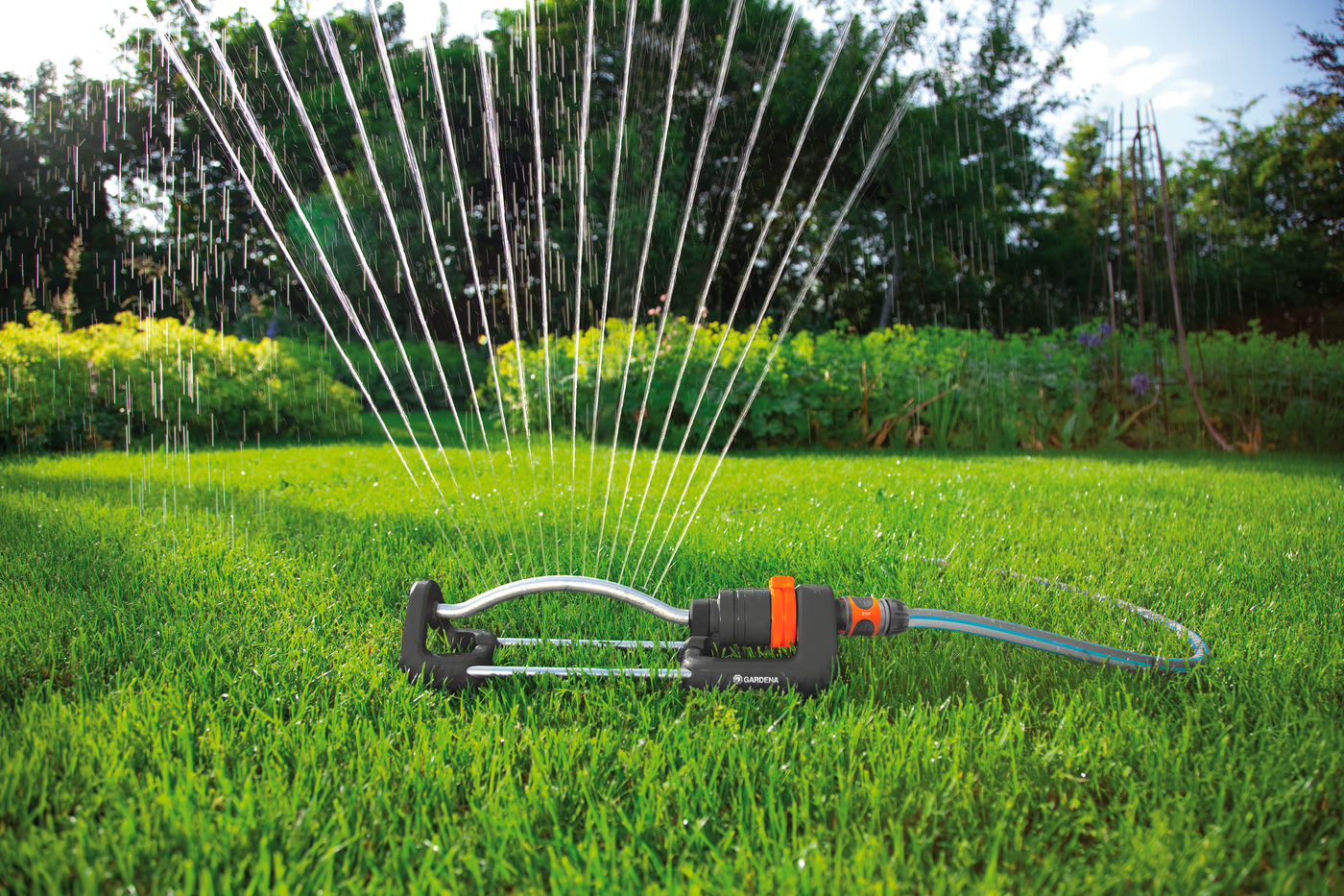 A Gardena oscillating sprinkler watering a lush green lawn in a garden setting.