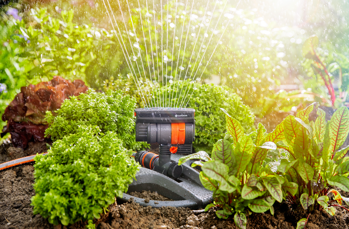 Gardena sprinkler watering a lush garden with various plants.