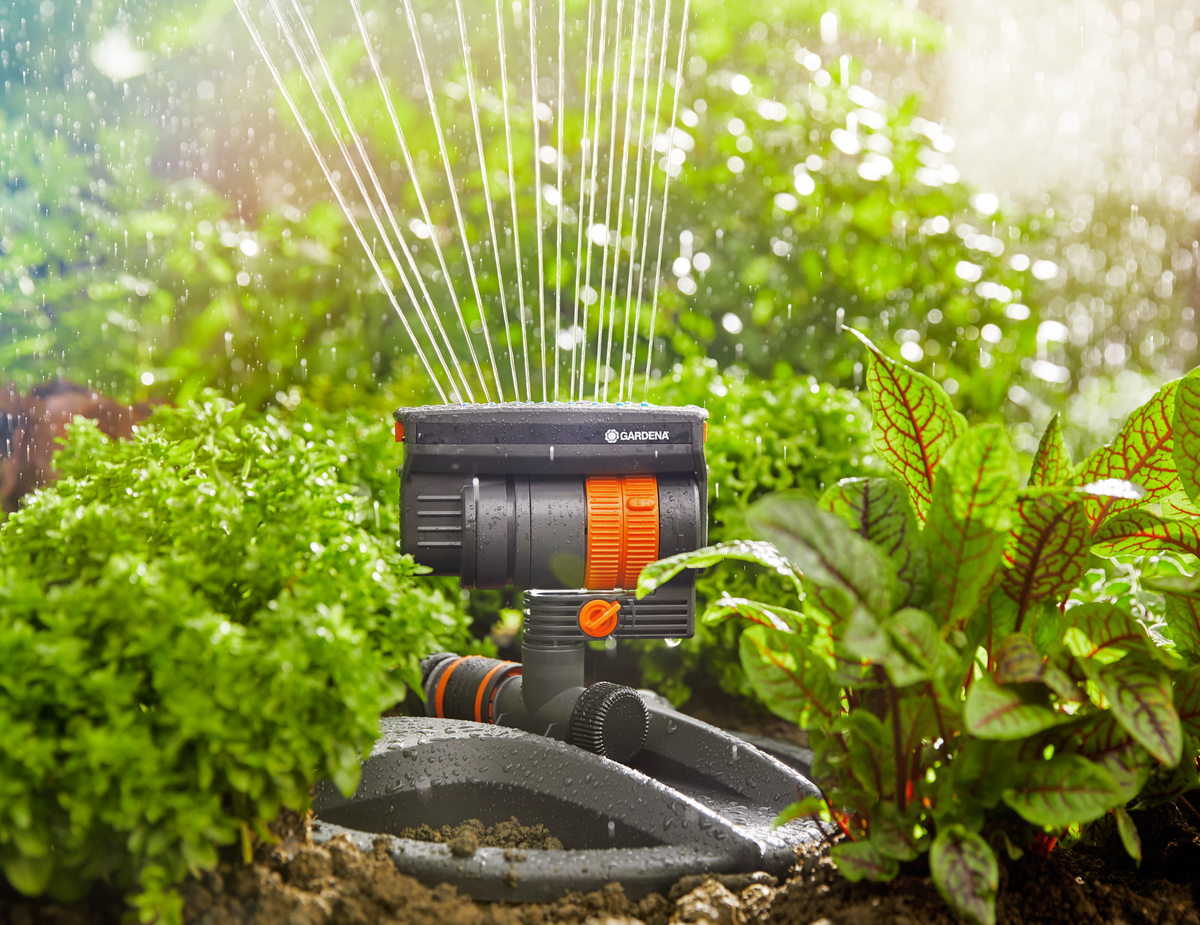 Gardena garden sprinkler in operation, watering plants with a lush green background.