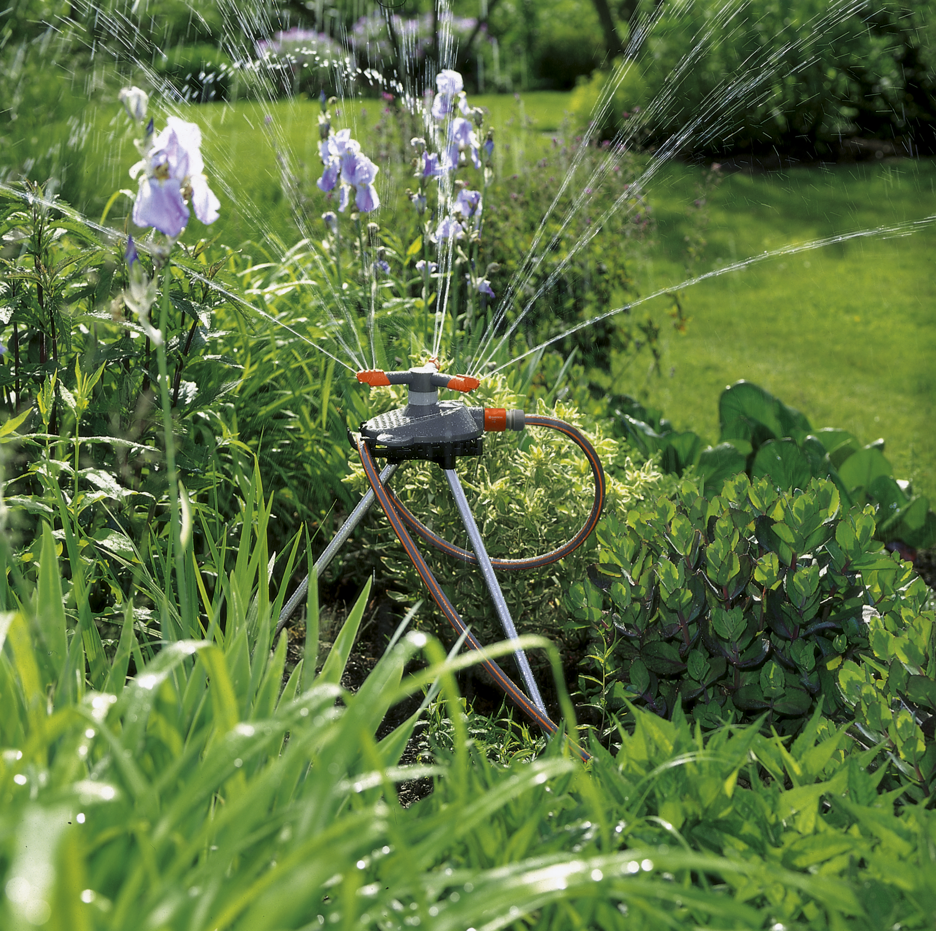 A garden sprinkler watering plants and flowers in a lush garden setting.
