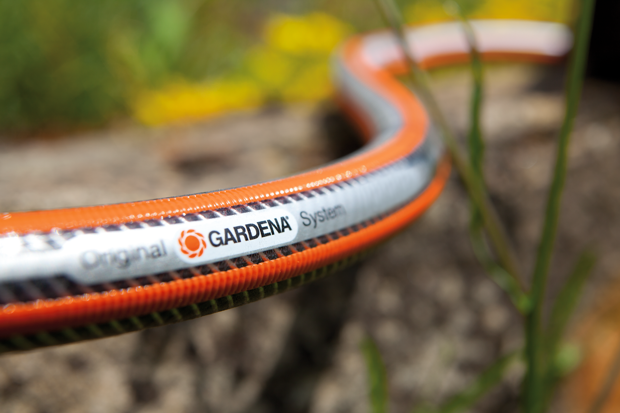 Close-up of a Gardena garden hose with branding, lying on a wooden surface outdoors.