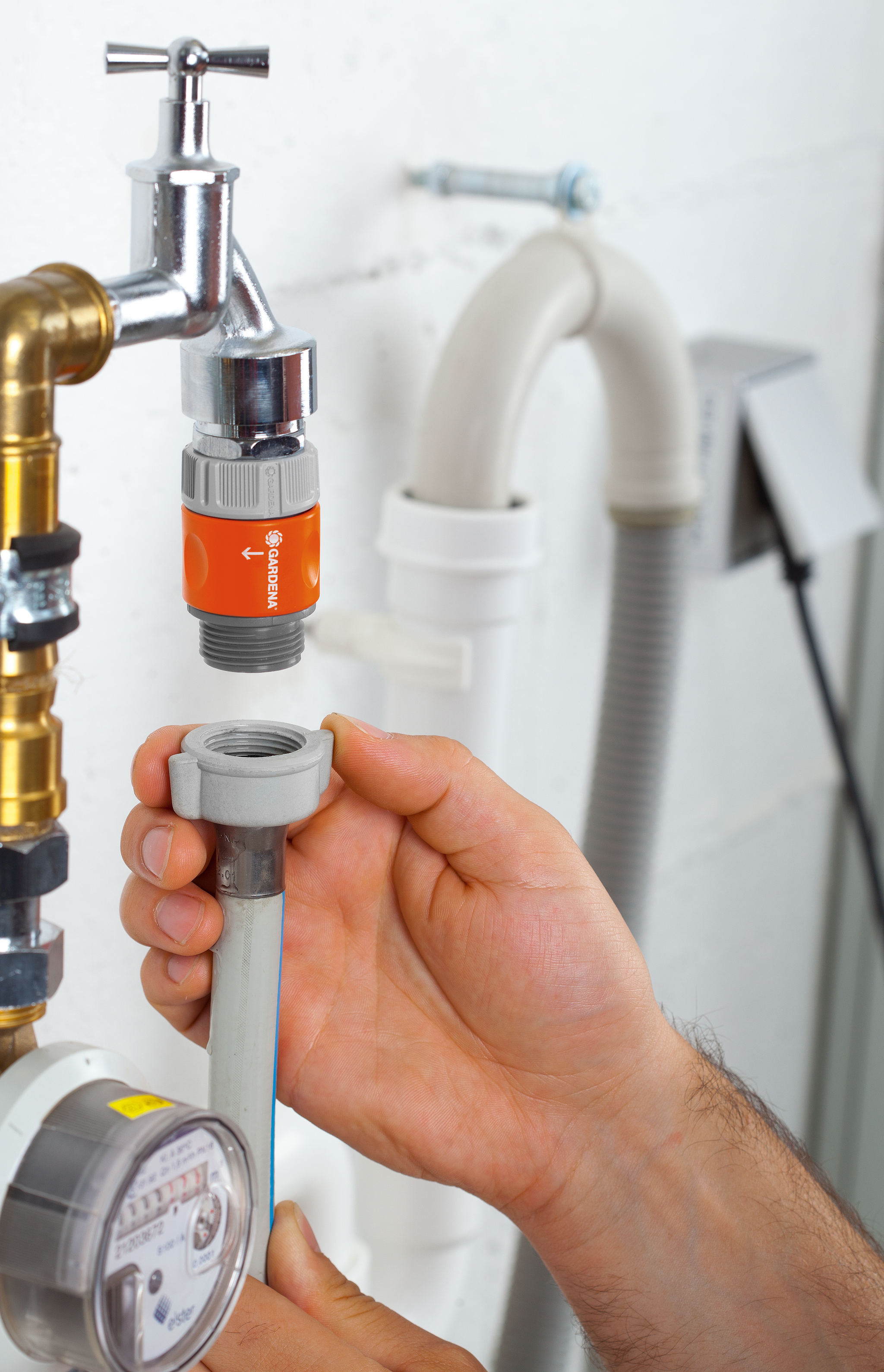 A person connecting a Gardena hose adapter to a water tap in a utility room.