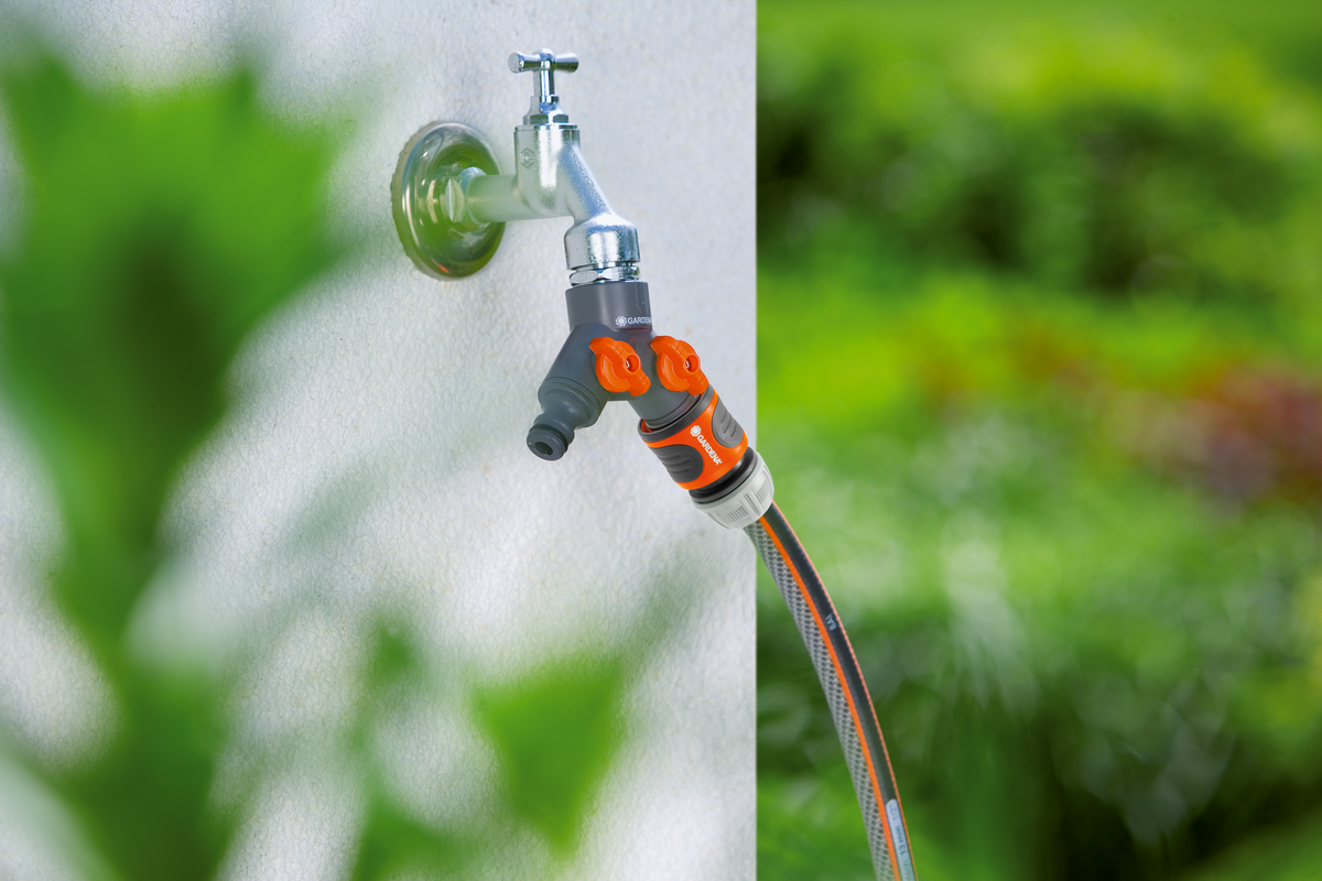 A garden hose connected to a dual tap adapter in a garden setting.