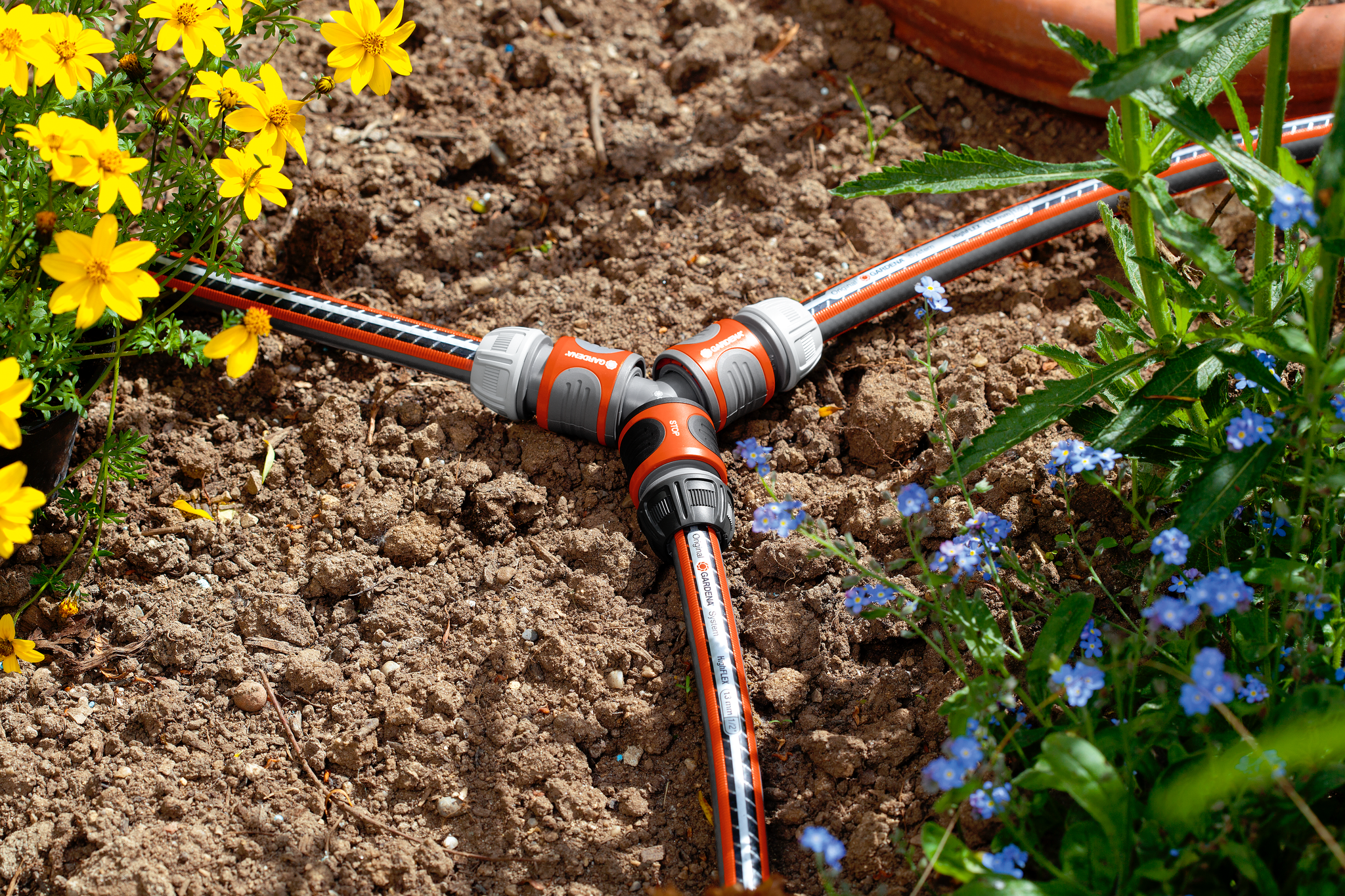 Gardena garden hose connector in a flower bed with yellow and blue flowers.