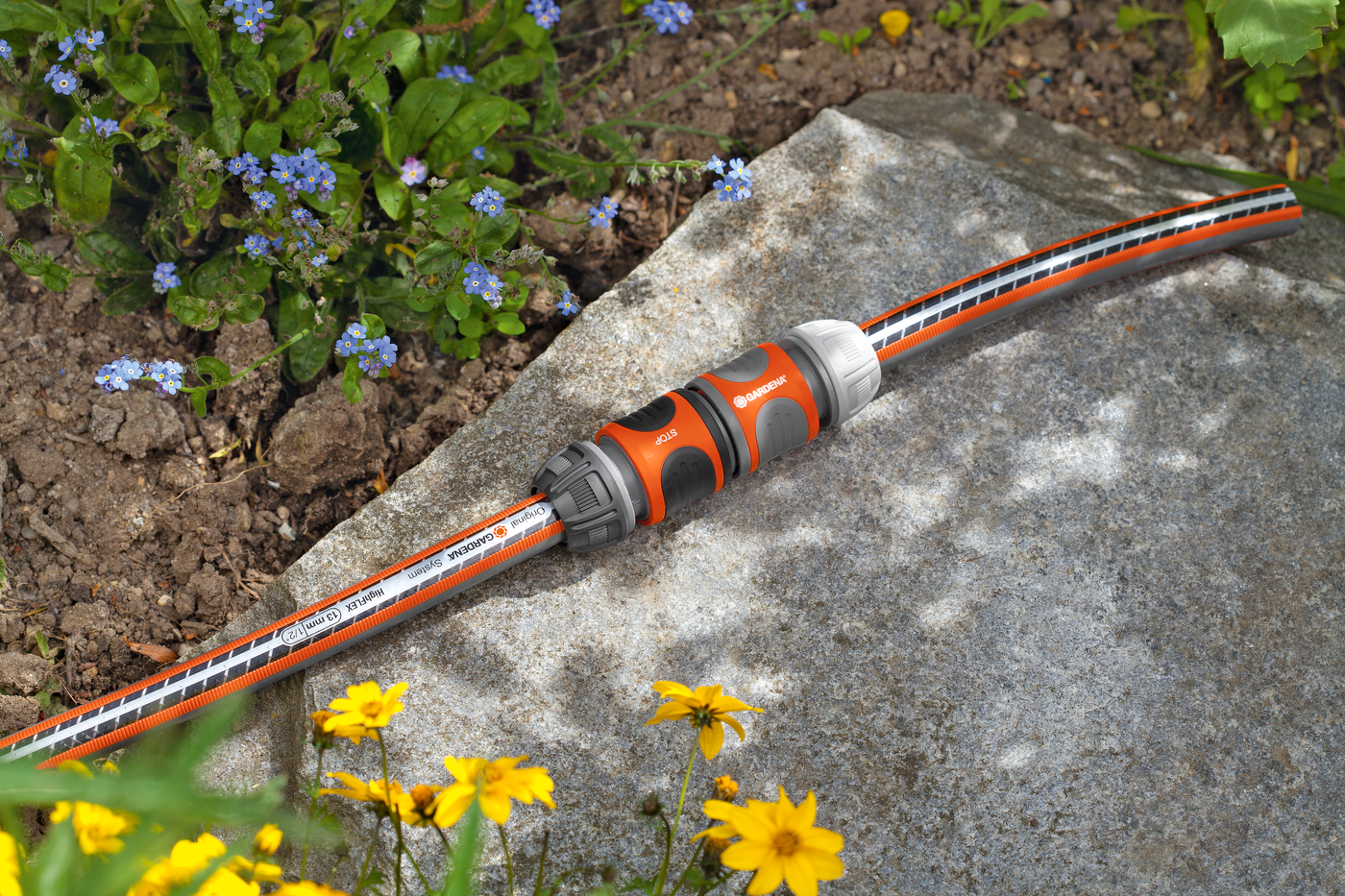 Gardena garden hose connector placed on a stone surface, surrounded by flowers.