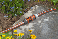 Gardena garden hose connector placed on a stone surface, surrounded by flowers., miniatuur 2