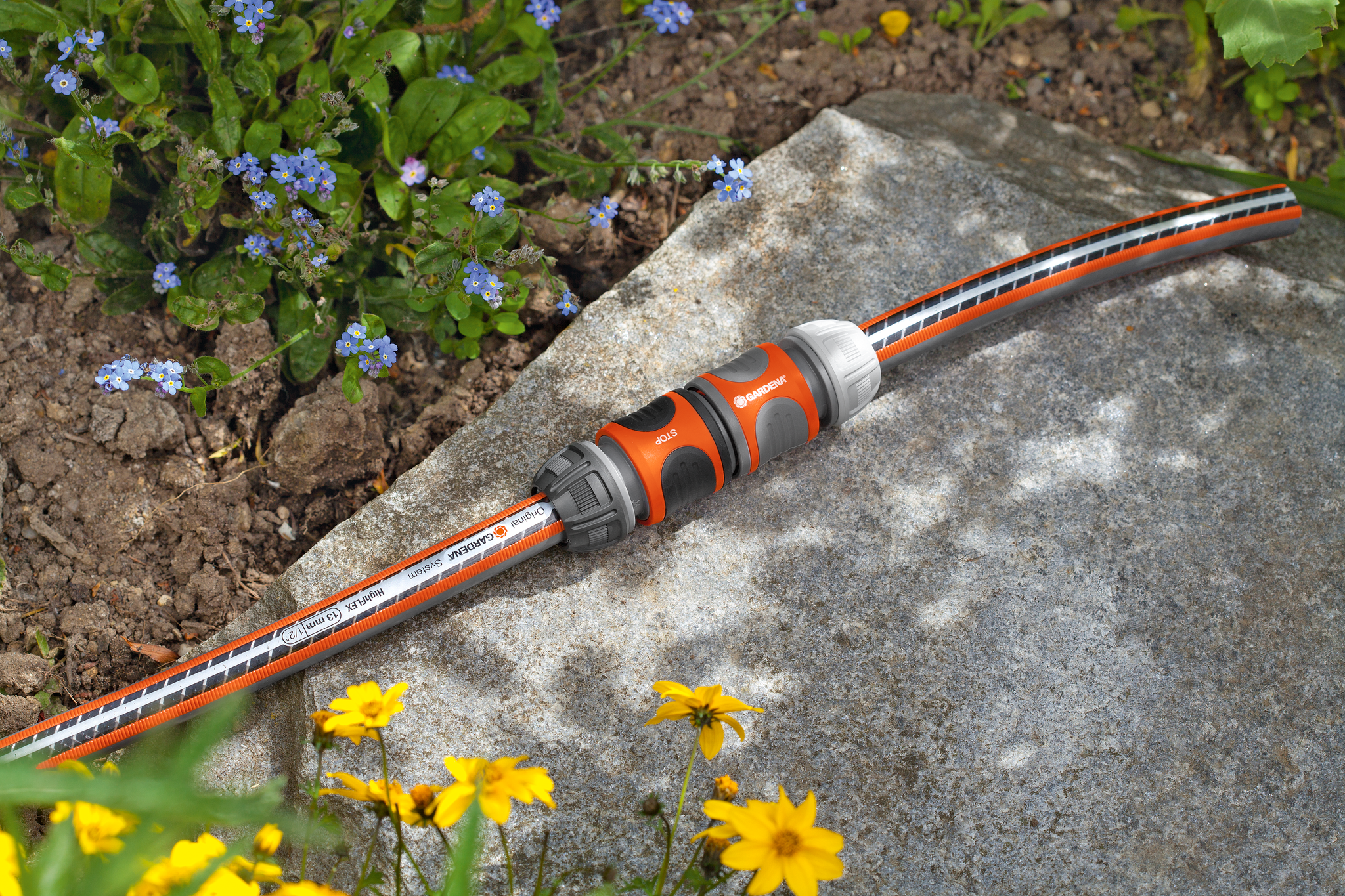 Gardena garden hose connector placed on a stone surface, surrounded by flowers.