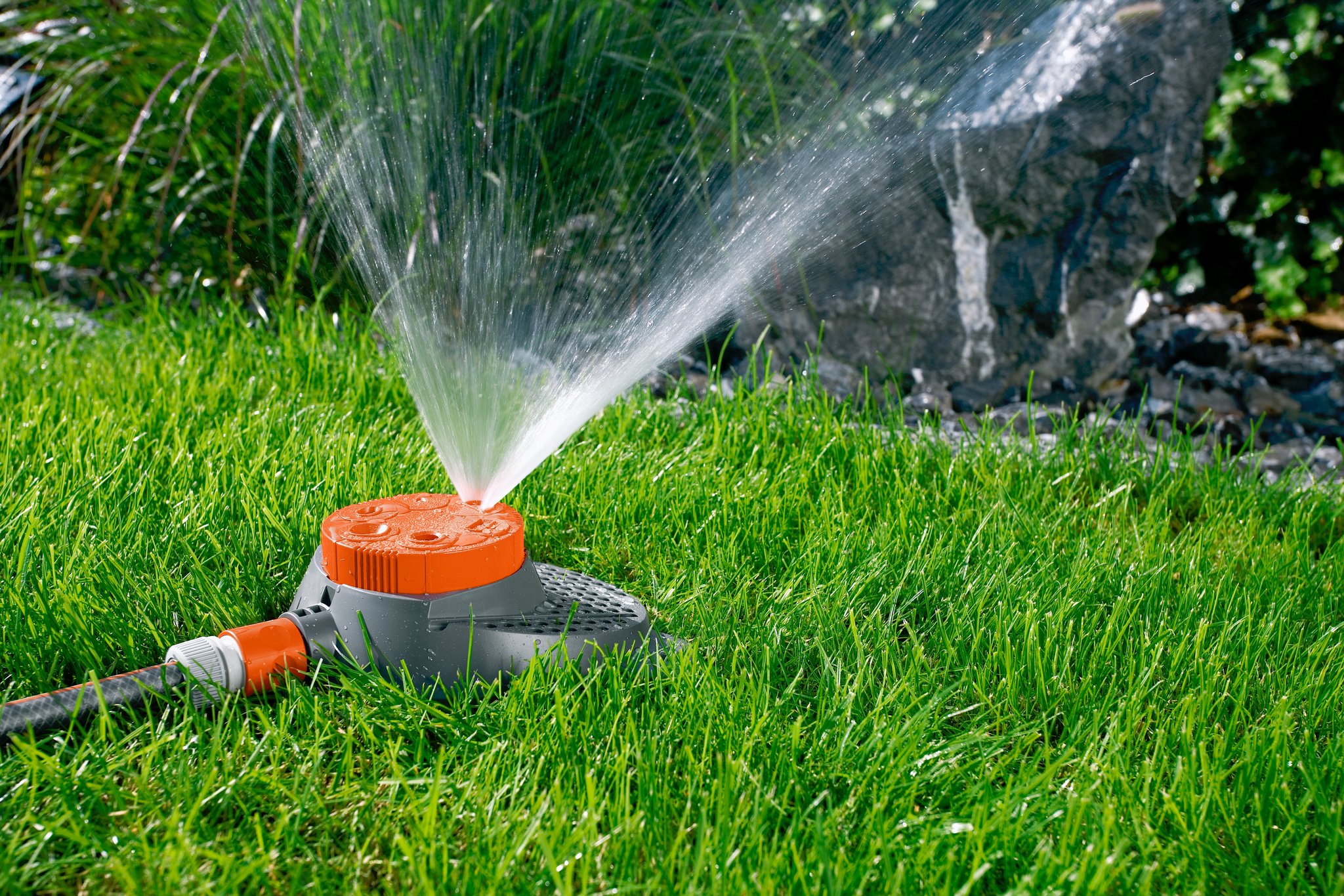 A garden sprinkler watering grass with a stone backdrop.