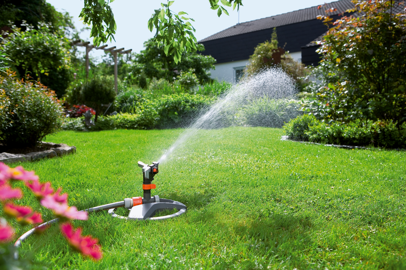 A garden sprinkler watering a lush green lawn with a house in the background., afbeelding 4 Sproeier