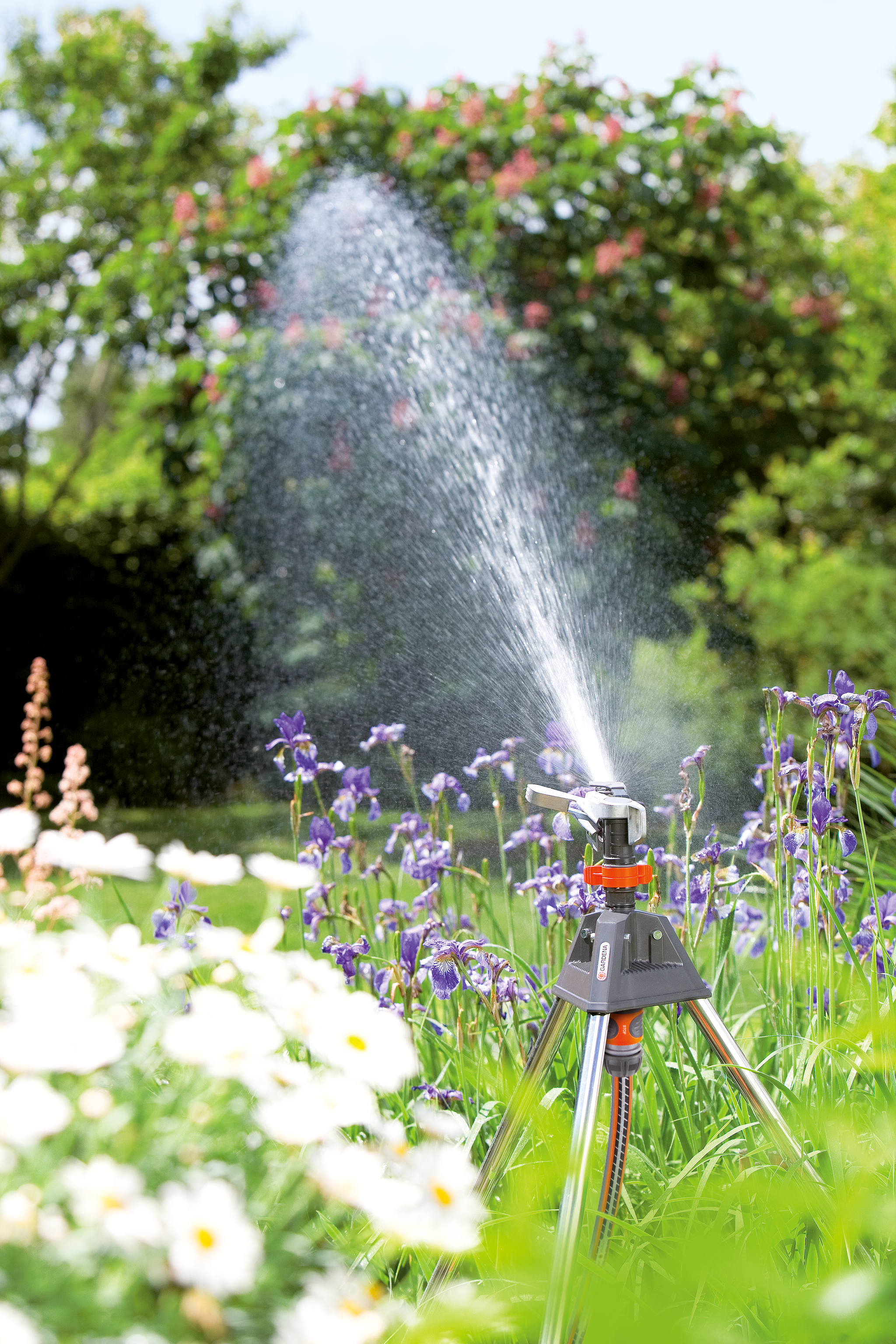 A garden sprinkler watering a flower bed with various blooming flowers.