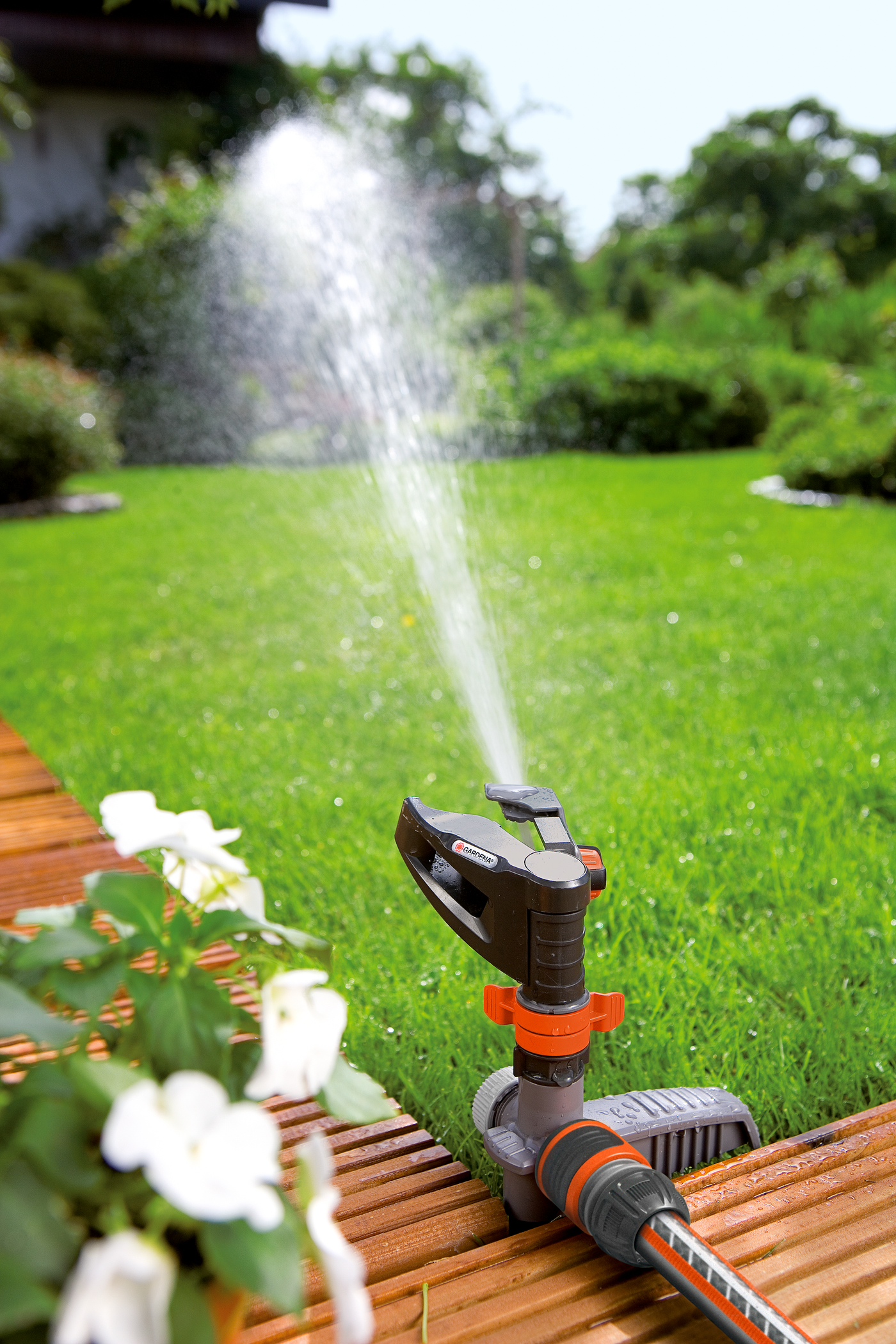 A Gardena sprinkler watering a lush green lawn next to a wooden deck.