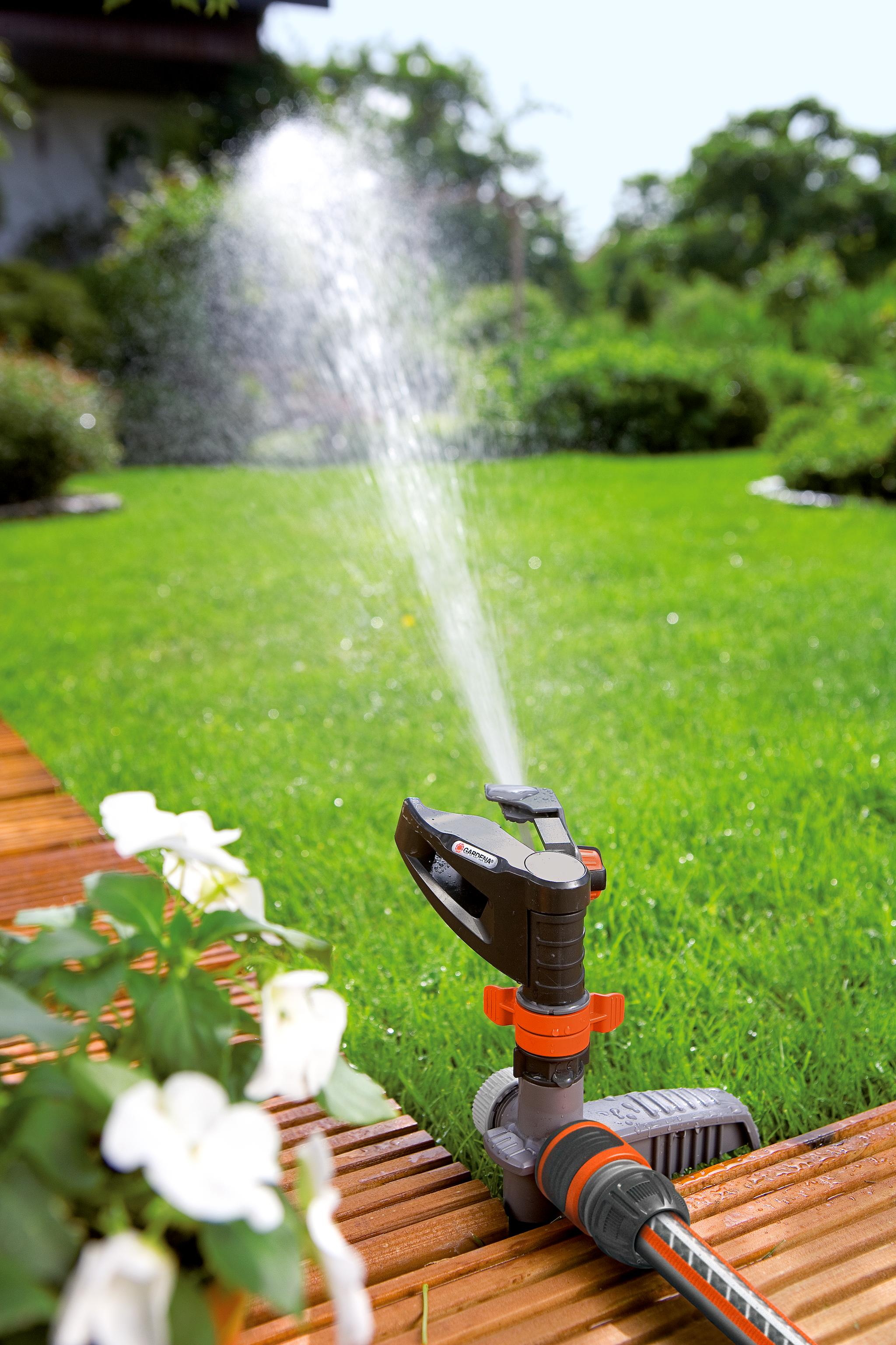 A Gardena sprinkler watering a lush green lawn next to a wooden deck.