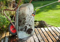 A person cleaning a wheelbarrow with a water hose on a wooden deck in a garden., miniatuur 3