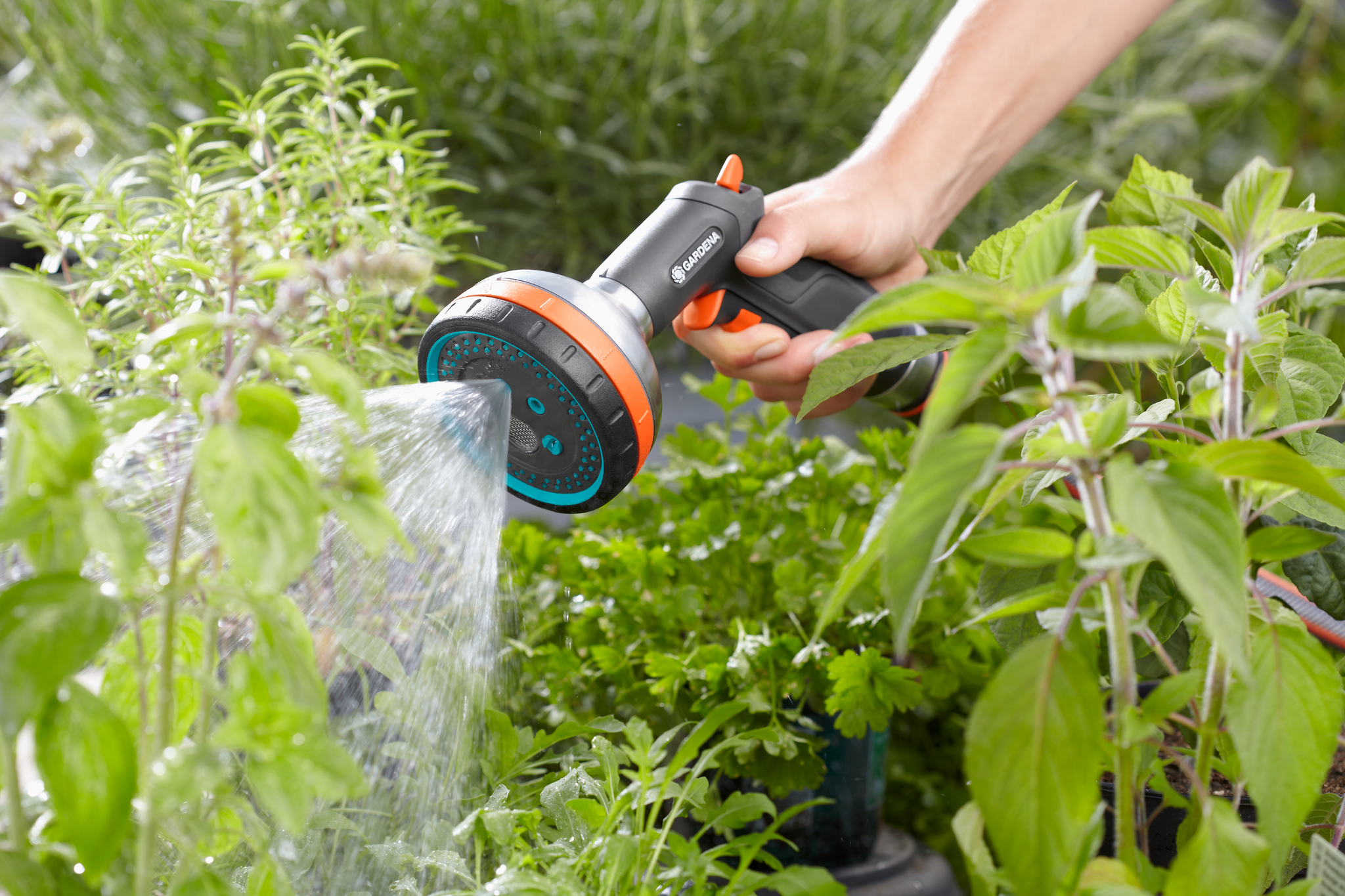 A person watering plants with a Gardena garden hose nozzle in a lush garden.