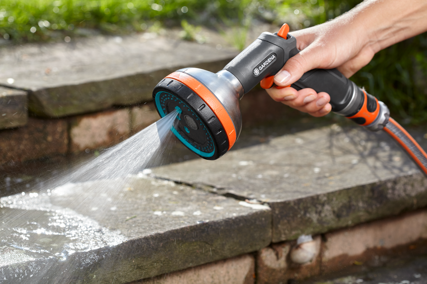 A person using a Gardena garden hose nozzle to spray water on stone steps.