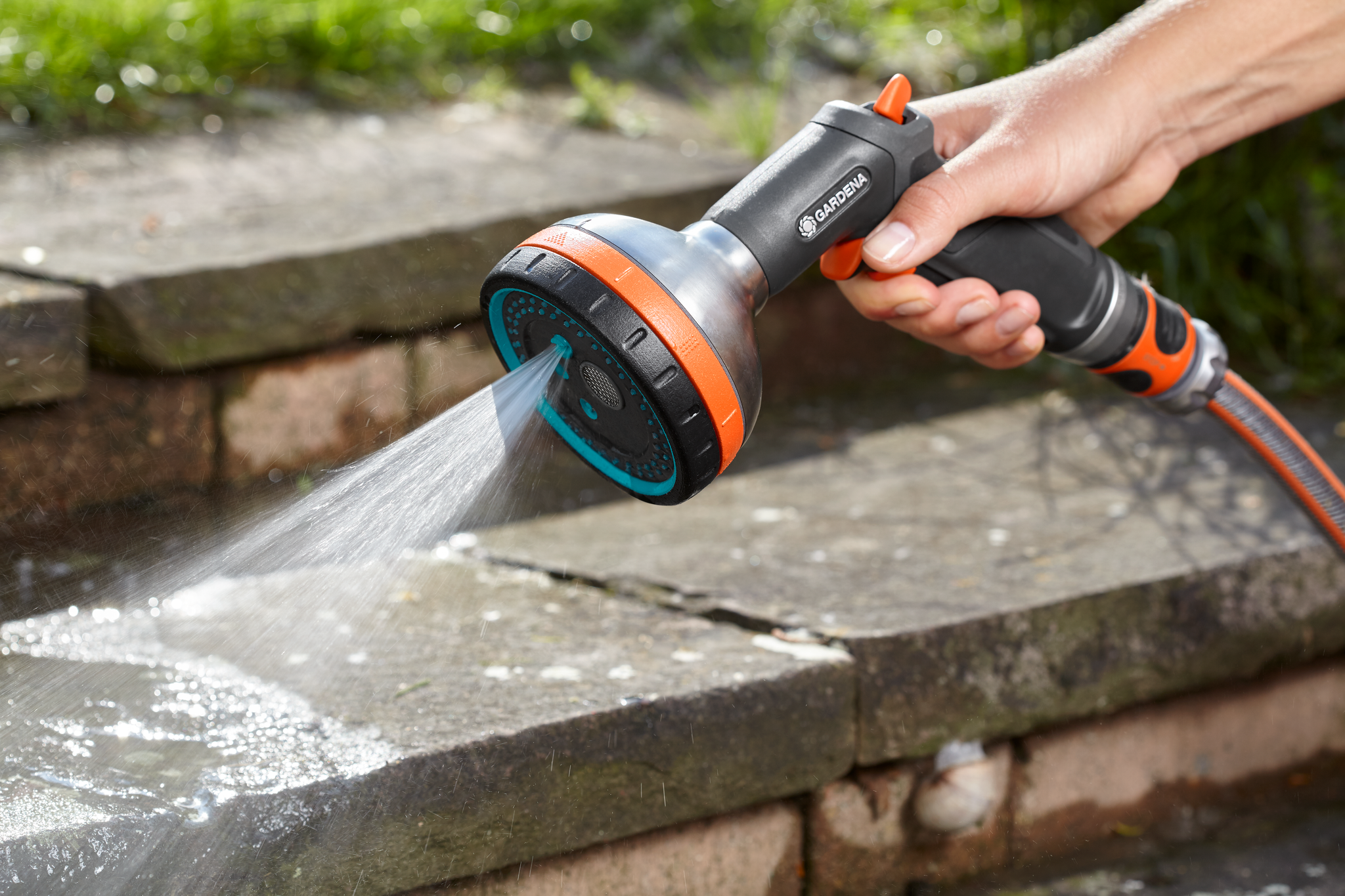 A person using a Gardena garden hose nozzle to spray water on stone steps.