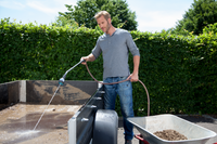 A person using a hose to clean a trailer bed, with a wheelbarrow filled with soil nearby., miniatuur 5