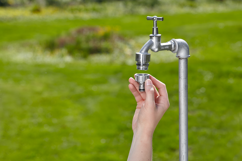 A person attaching a connector to an outdoor water tap in a garden setting., afbeelding 4 Slangaccessoire