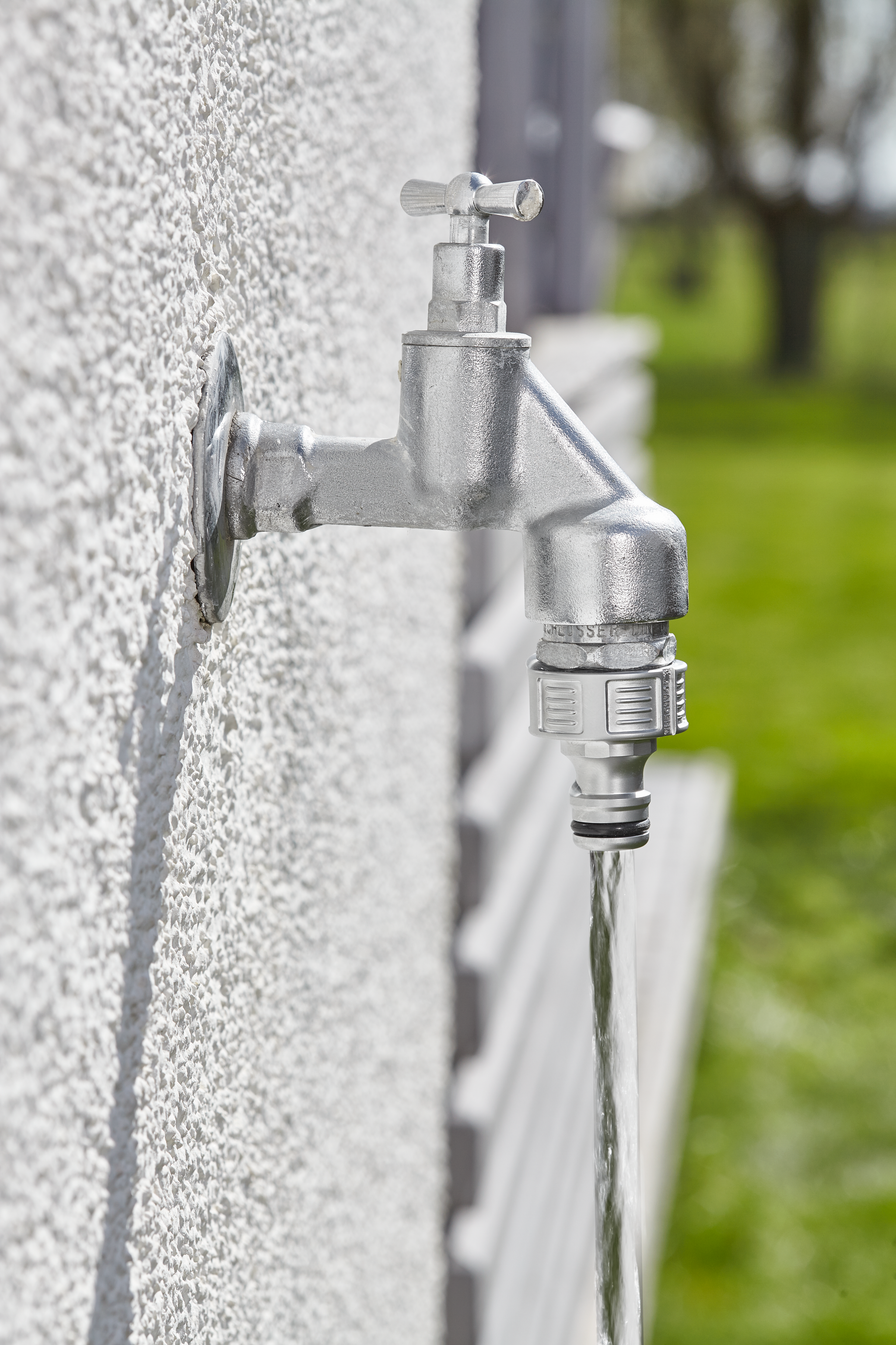 Outdoor water tap with a hose connector attached, water flowing from the tap.