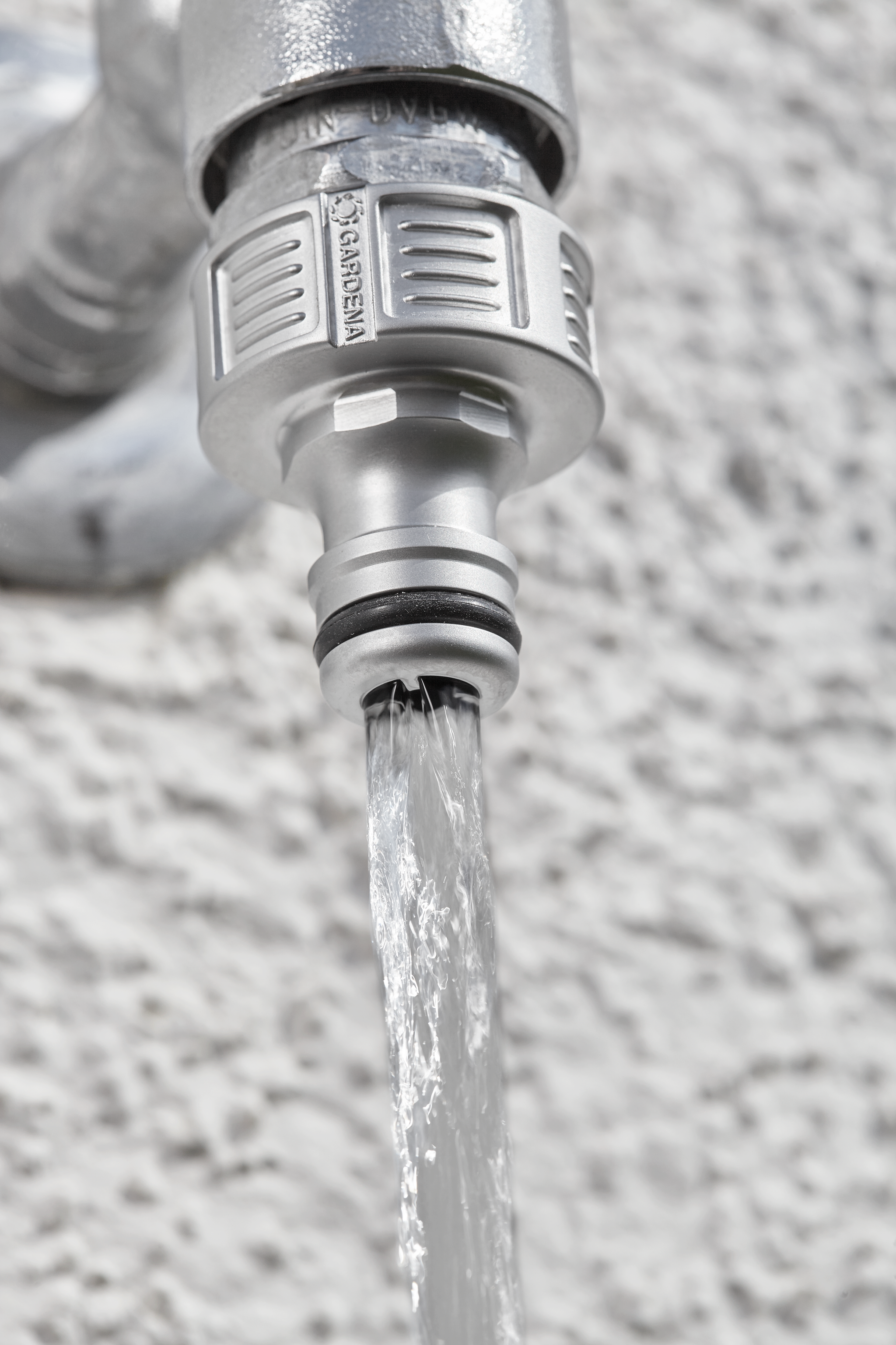 Close-up of a Gardena hose connector attached to a water tap with water flowing out.