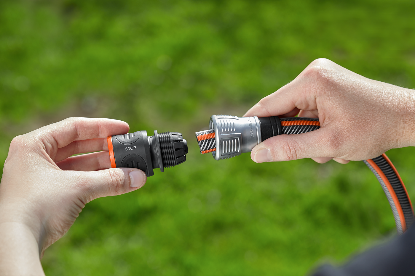 Two hands connecting a Gardena hose with a stop valve in a garden setting.