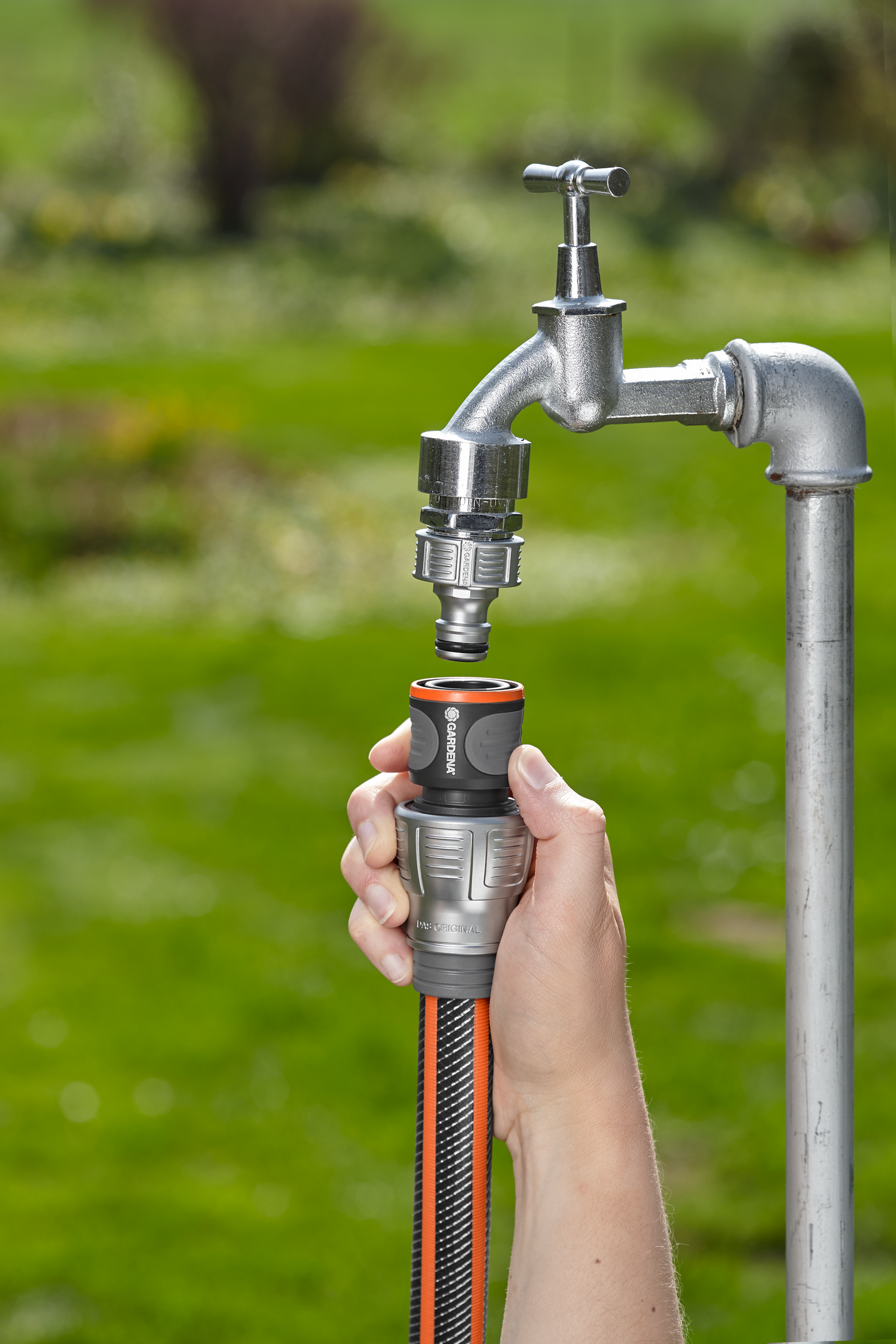 A person connecting a Gardena hose to an outdoor water tap in a garden.